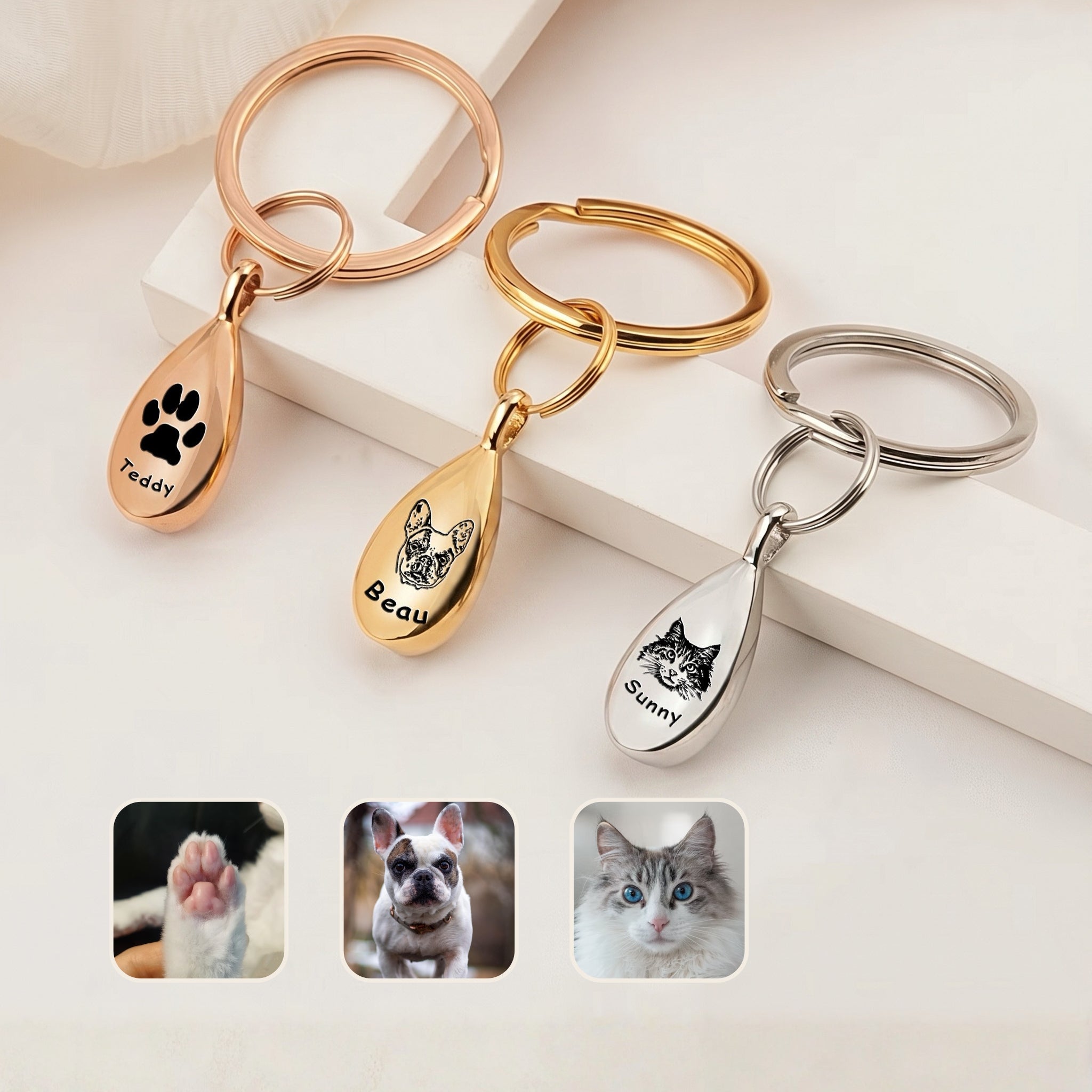 Pet portrait ashes teardrop keychain shown in all three finishes &mdash; rhodium silver, 18k gold, and 18k rose gold teardrop pendants engraved with hand-drawn pet portraits and names, staged on cream blocks with reference photo insets