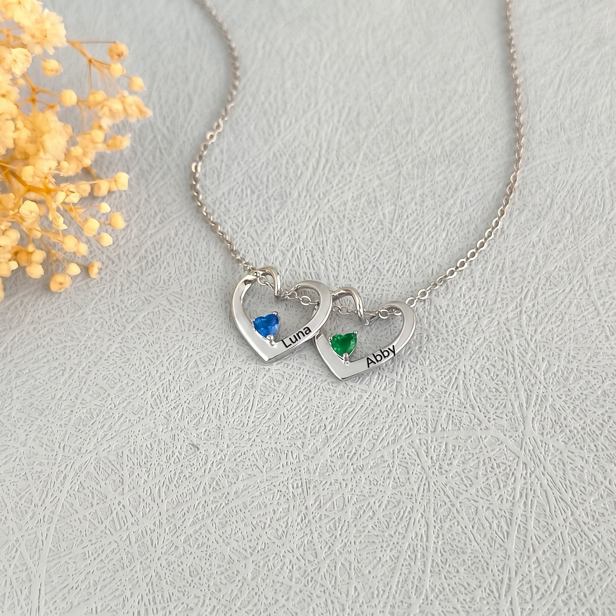 Two rhodium-plated heart pendants with engraved pet names and colored birthstones on a delicate chain