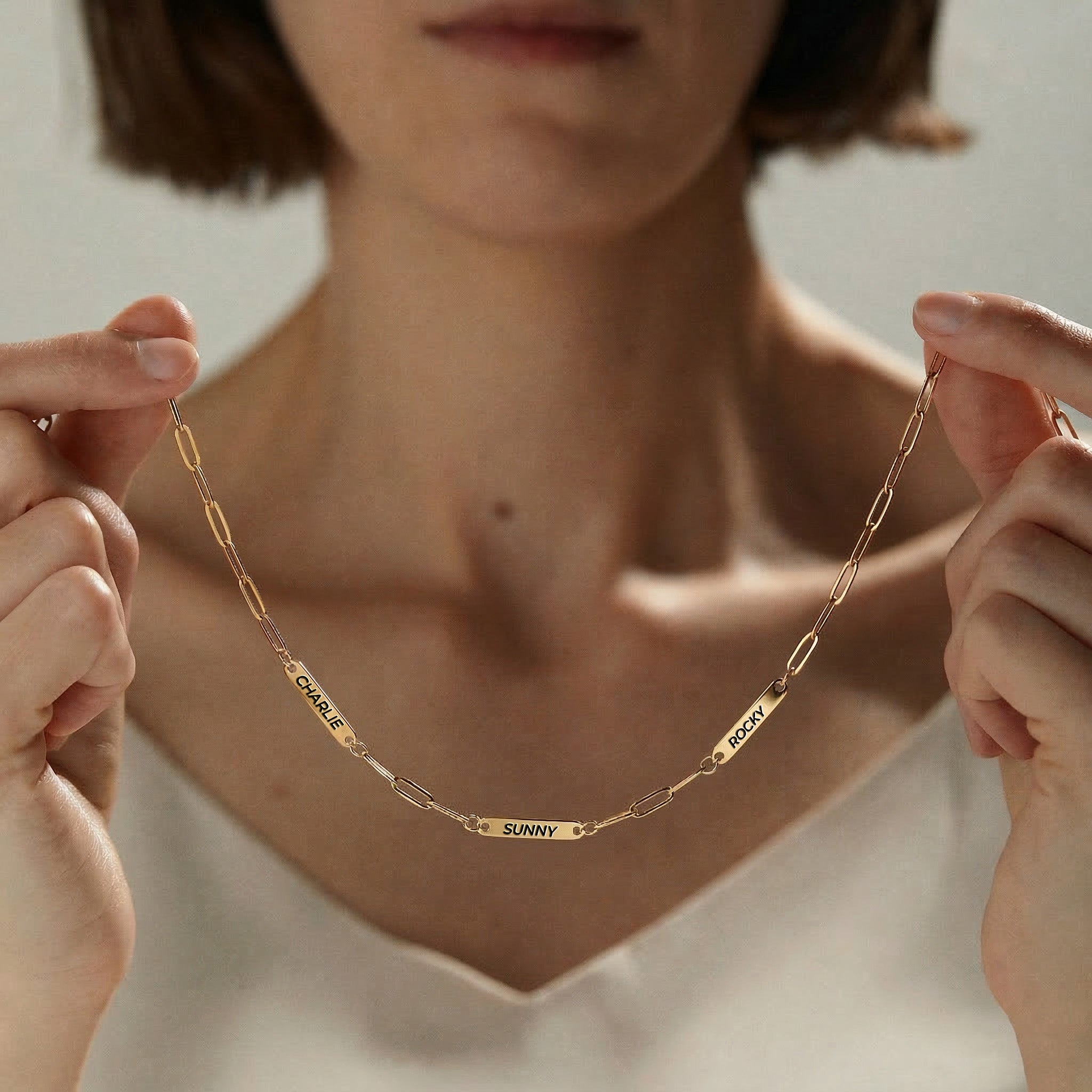 Gold paperclip chain necklace with three engraved pet name bars worn at the collarbone