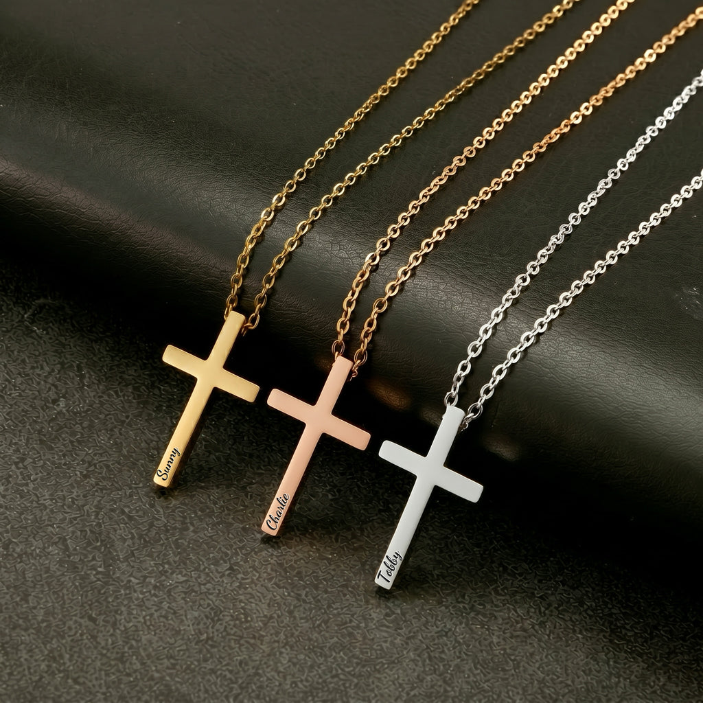 Three personalized cross necklaces in gold, rose gold, and silver, each engraved with a pet name, laid on dark surface