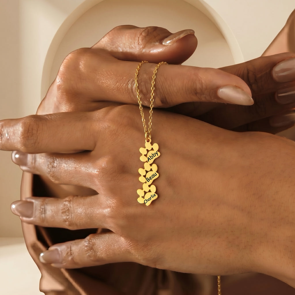 Three gold paw print pendants stacked vertically, each engraved with a pet name