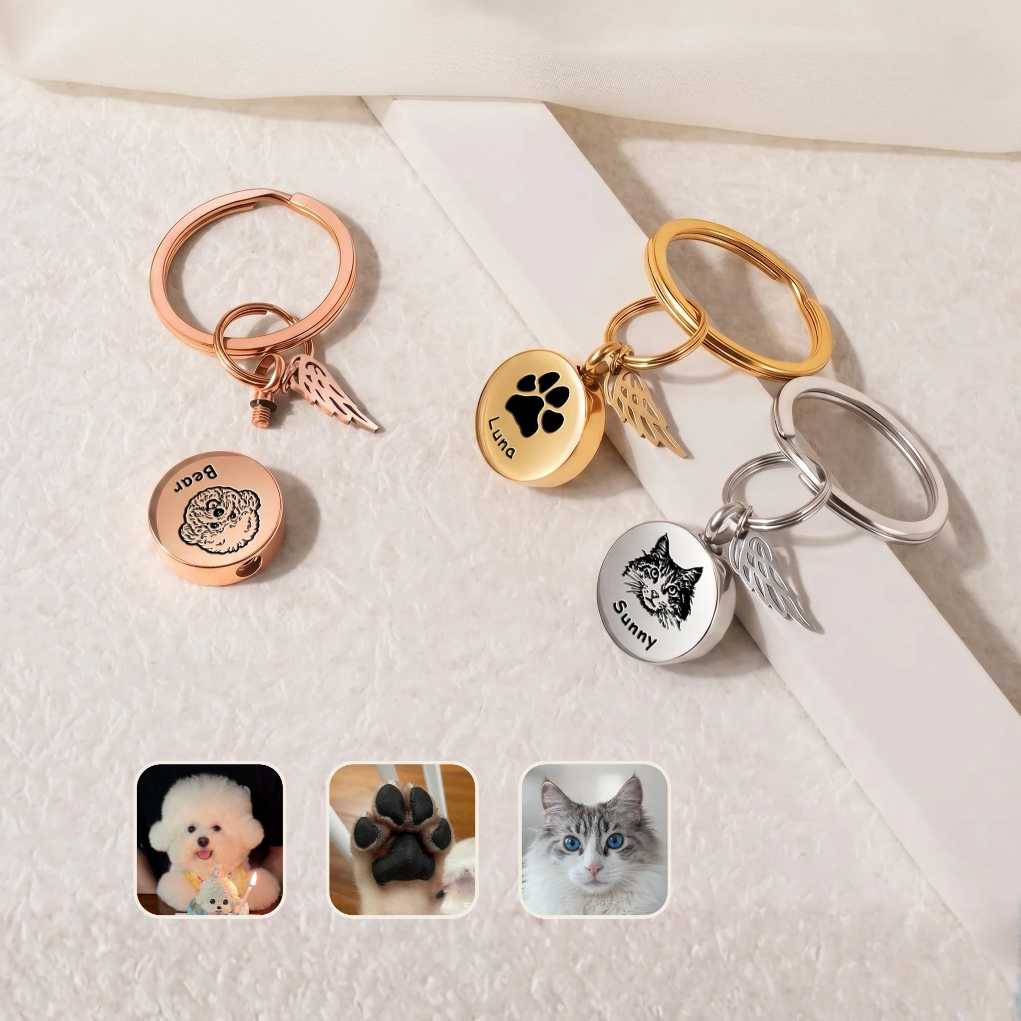 Pet cremation disc keychain shown in all three plating finishes &mdash; rose gold, rhodium silver, and 18k gold &mdash; staged on a pale surface with small pet reference photo insets, demonstrating both portrait + name and paw-print + name engraving options on the screw-top disc face plus permanently-attached angel-wing memorial charm