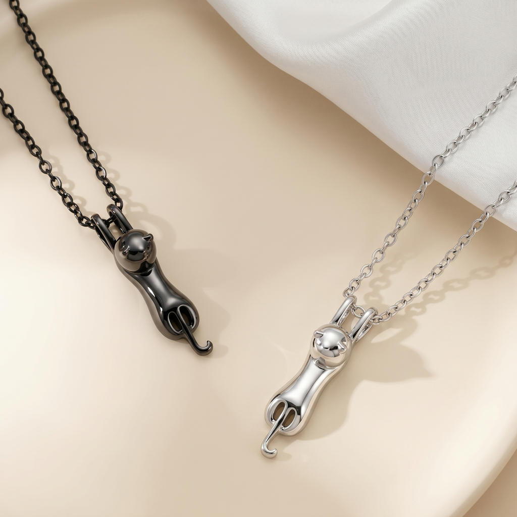 Black and rhodium cat urn pendant necklaces side by side on cream backdrop, alternate angle