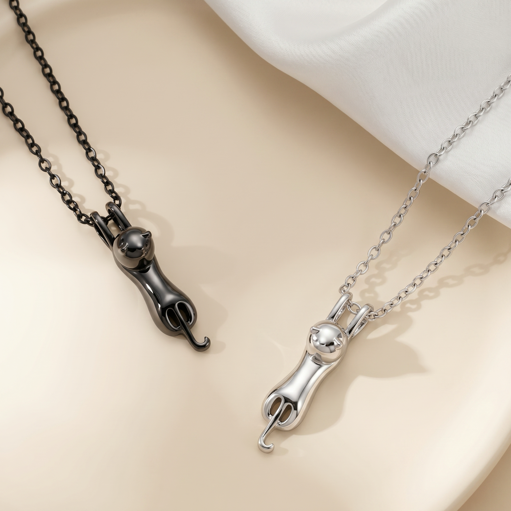 Black and rhodium cat urn pendant necklaces side by side on cream backdrop, alternate angle