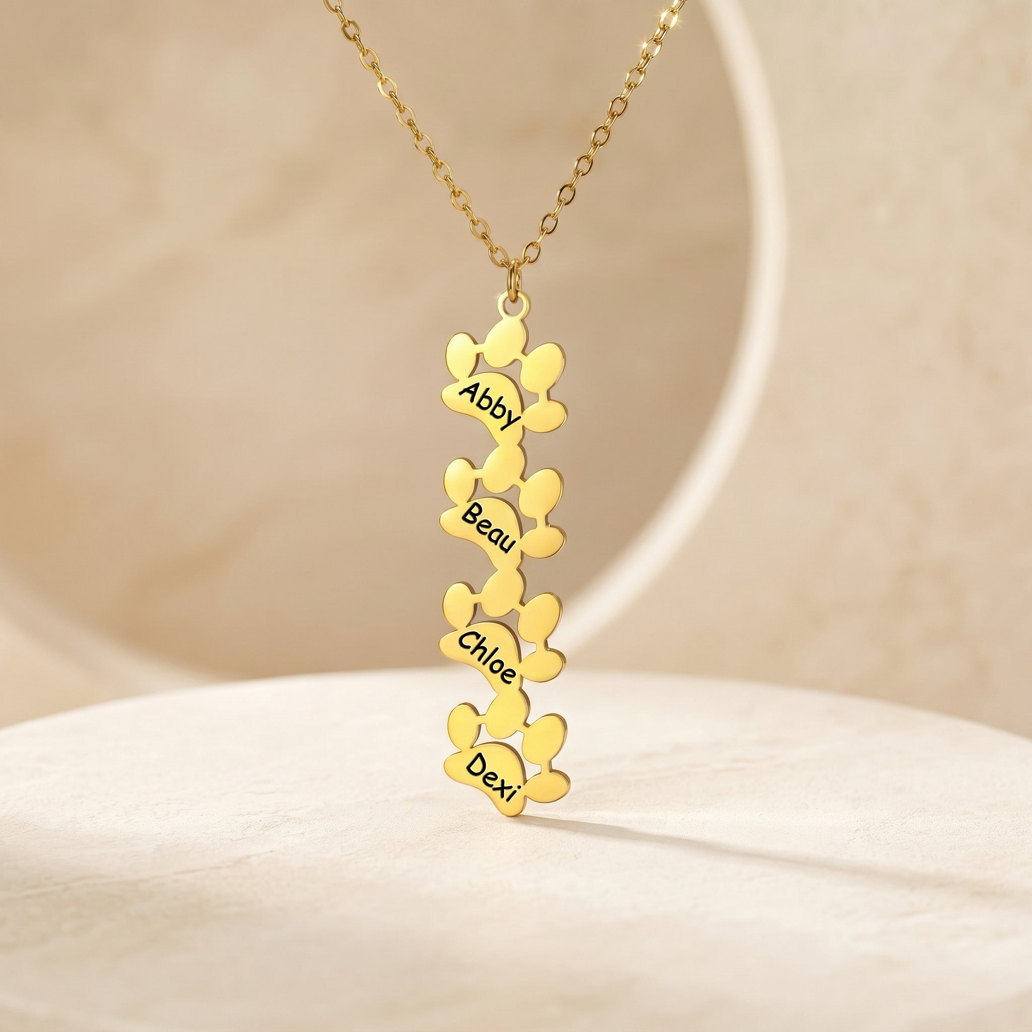 Four gold paw pendants with names Abby Beau Chloe Dexi on cream stand