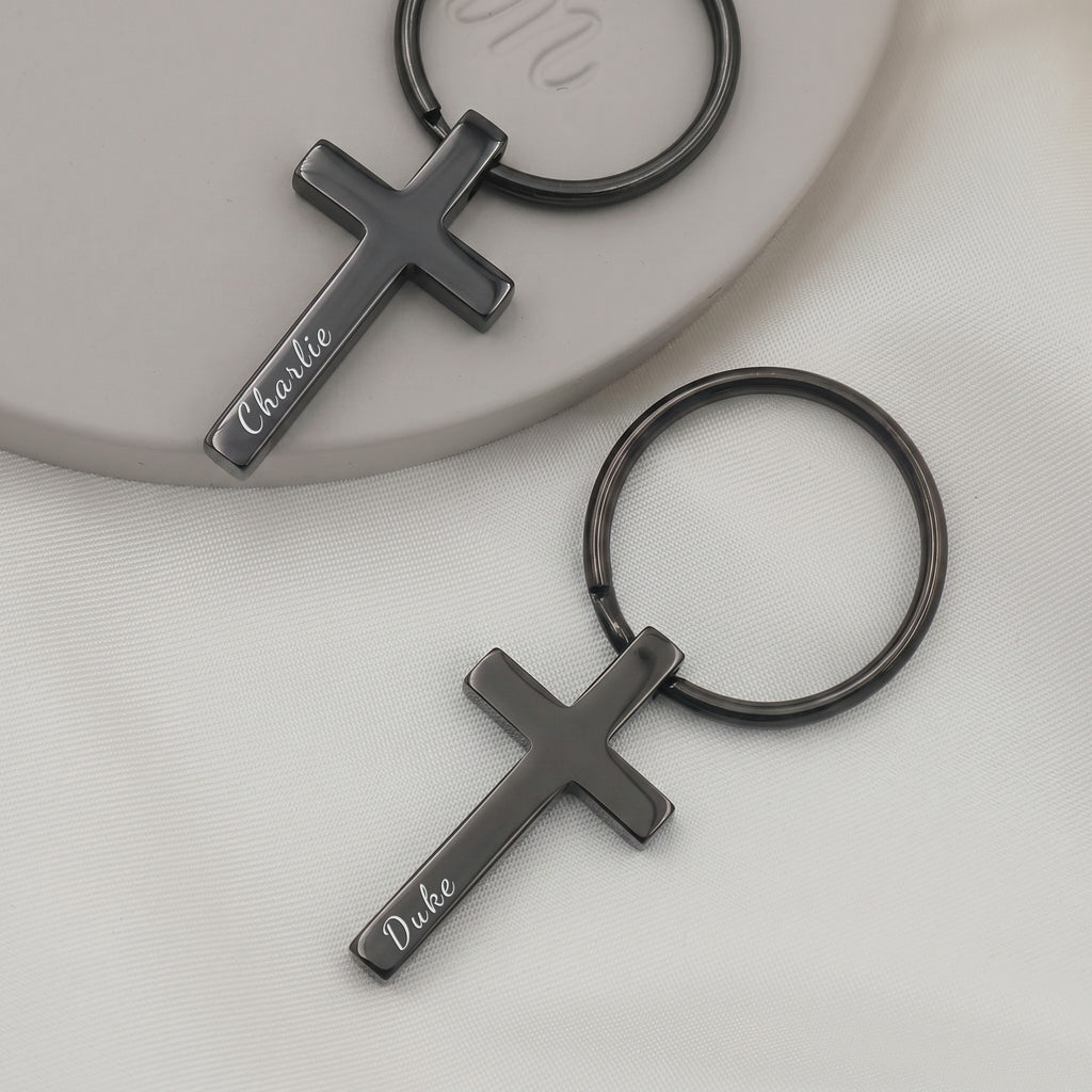 Matte black pet cross keychain pair on ceramic tray with soft fabric — solemn quieter finish, front-face pet name engraving visible