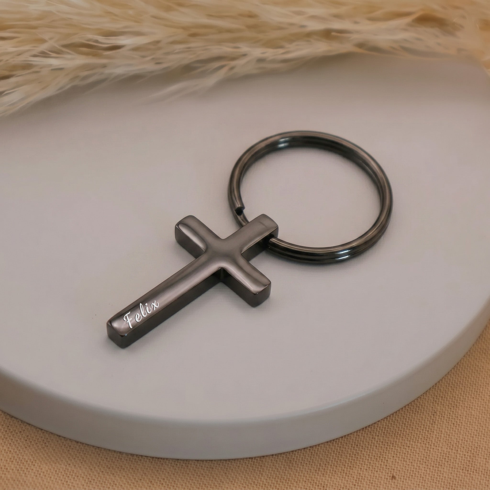 Matte black pet cross keychain single close-up on a ceramic tray — engraving detail visible on the dark plated cross face