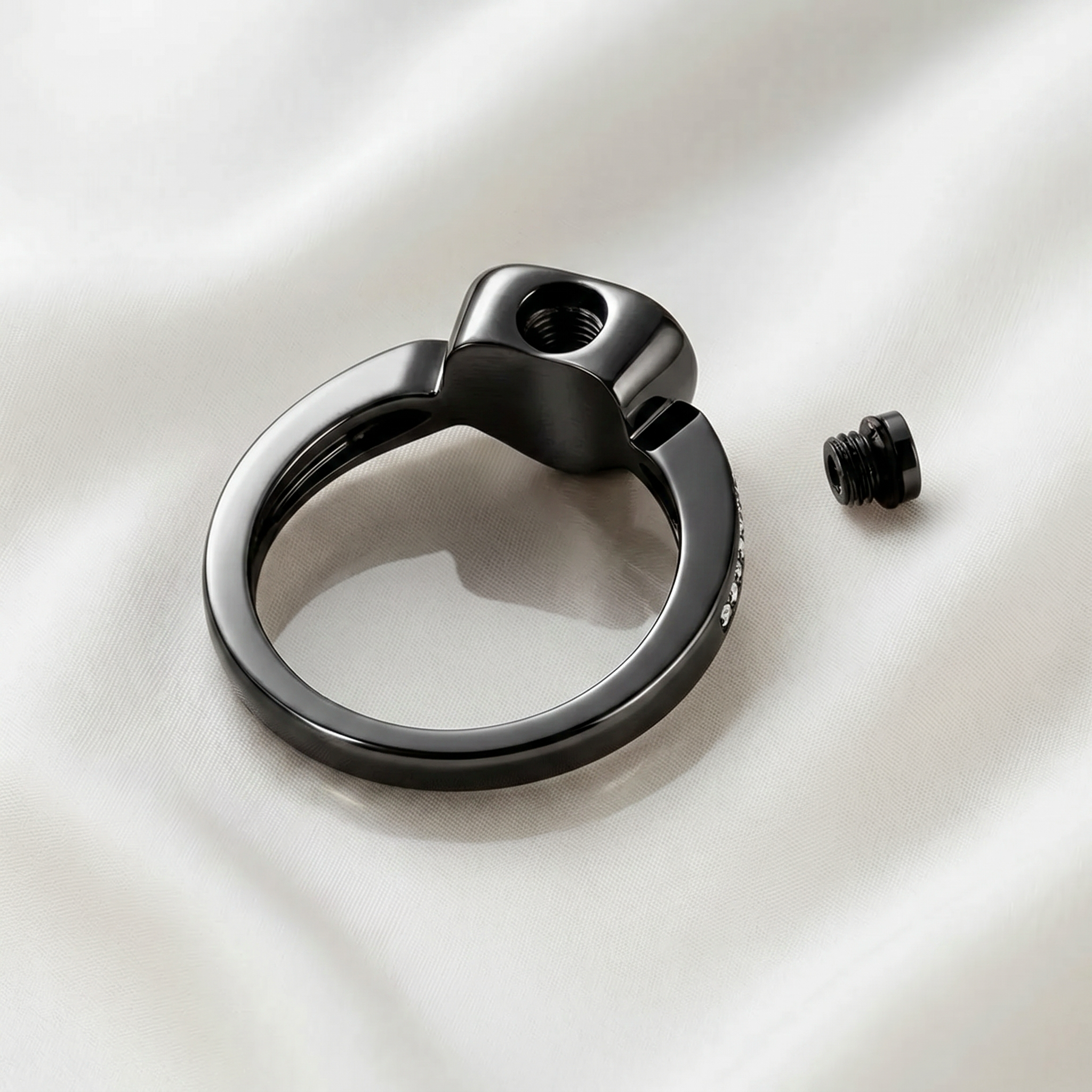 Back of black heart urn ring showing threaded fill hole with screw removed, ashes chamber visible