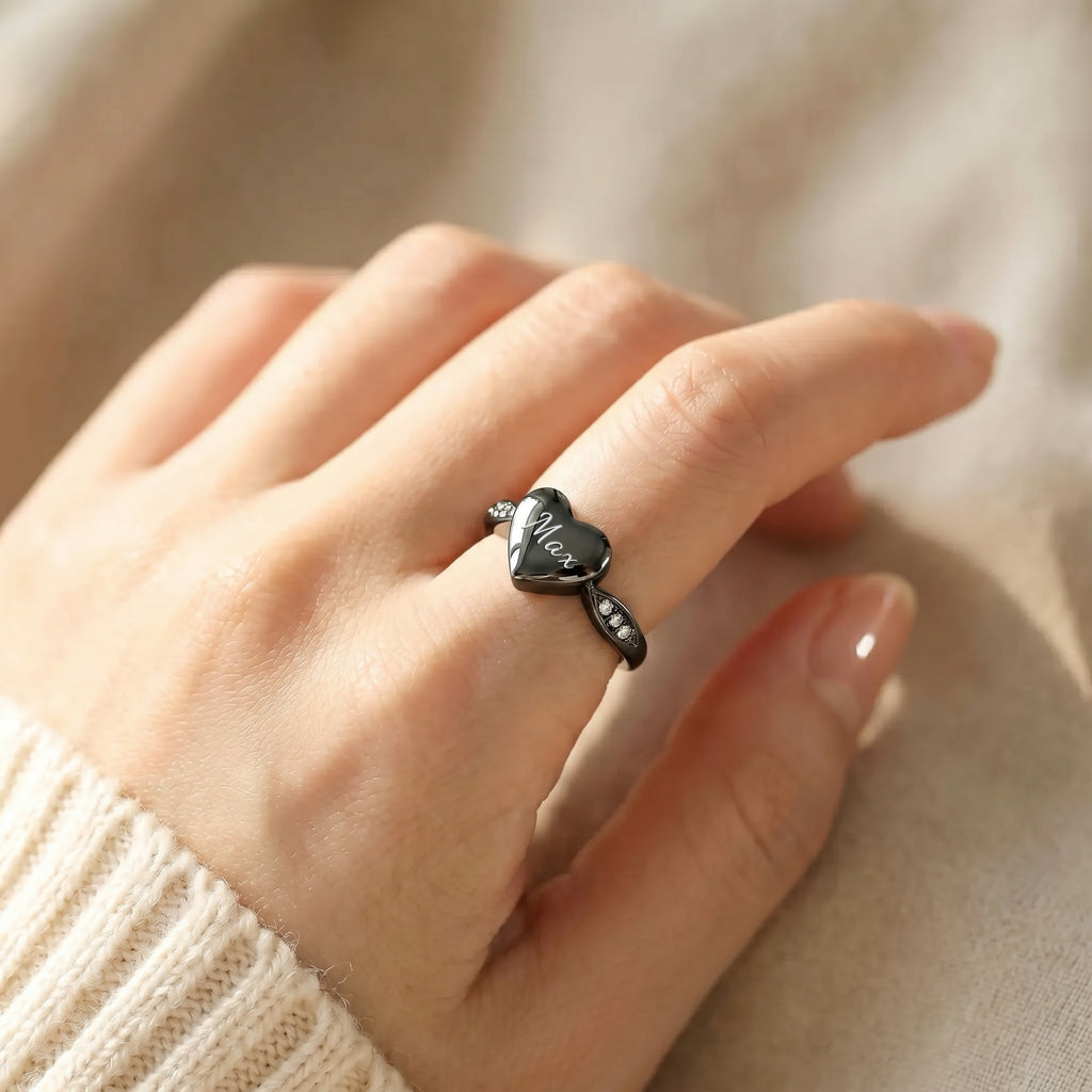 Black heart urn ring worn on a hand, white script engraving on heart face, CZ stones catching light