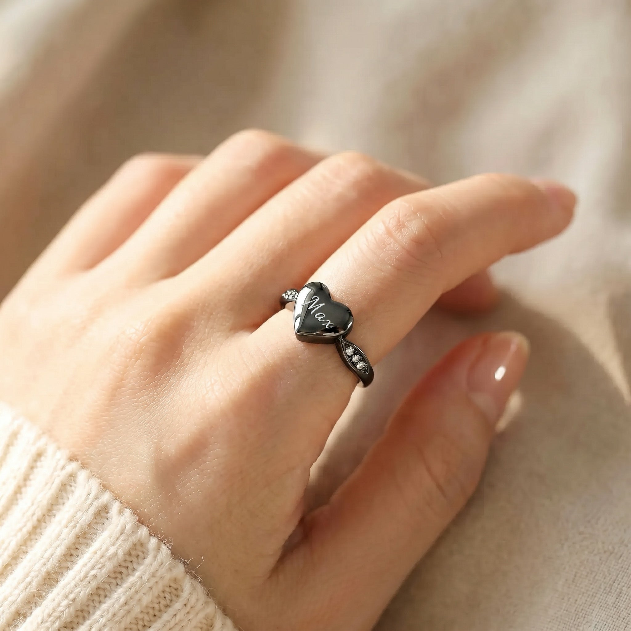 Black heart urn ring worn on a hand, white script engraving on heart face, CZ stones catching light