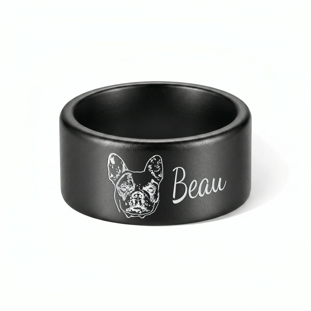 Single matte black wide band pet ring on a near-white background, engraved portrait and script name