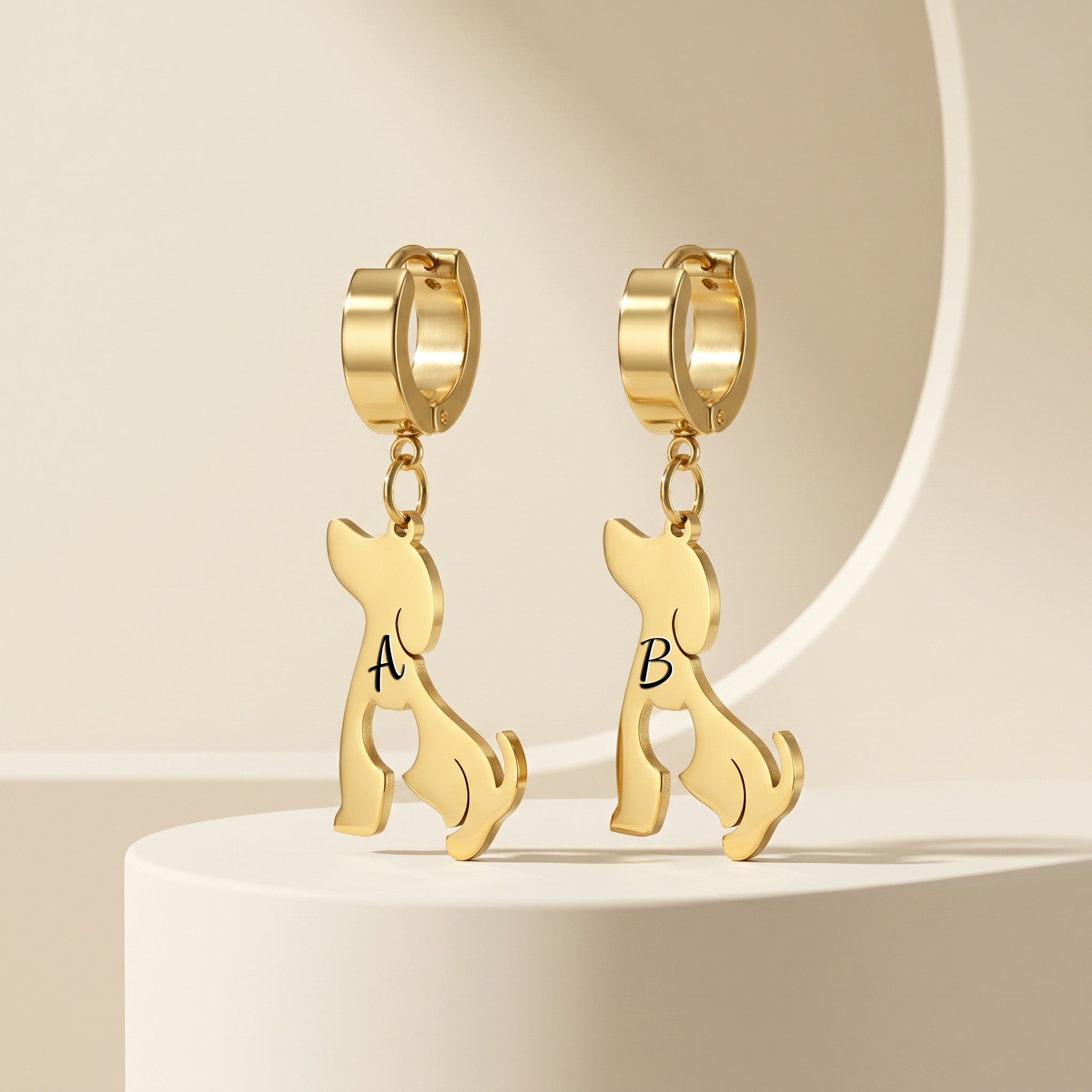 Pair of gold dog-silhouette name earrings on a cream pedestal