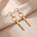 Pair of gold pet name bar drop earrings engraved with a pet's name in block letters, on cream fabric