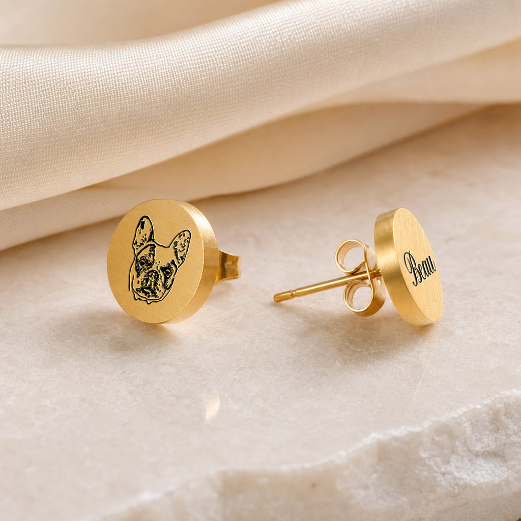 Gold pet portrait stud earrings as a pair, hand-drawn pet portrait on one stud and name in script on the other, on marble