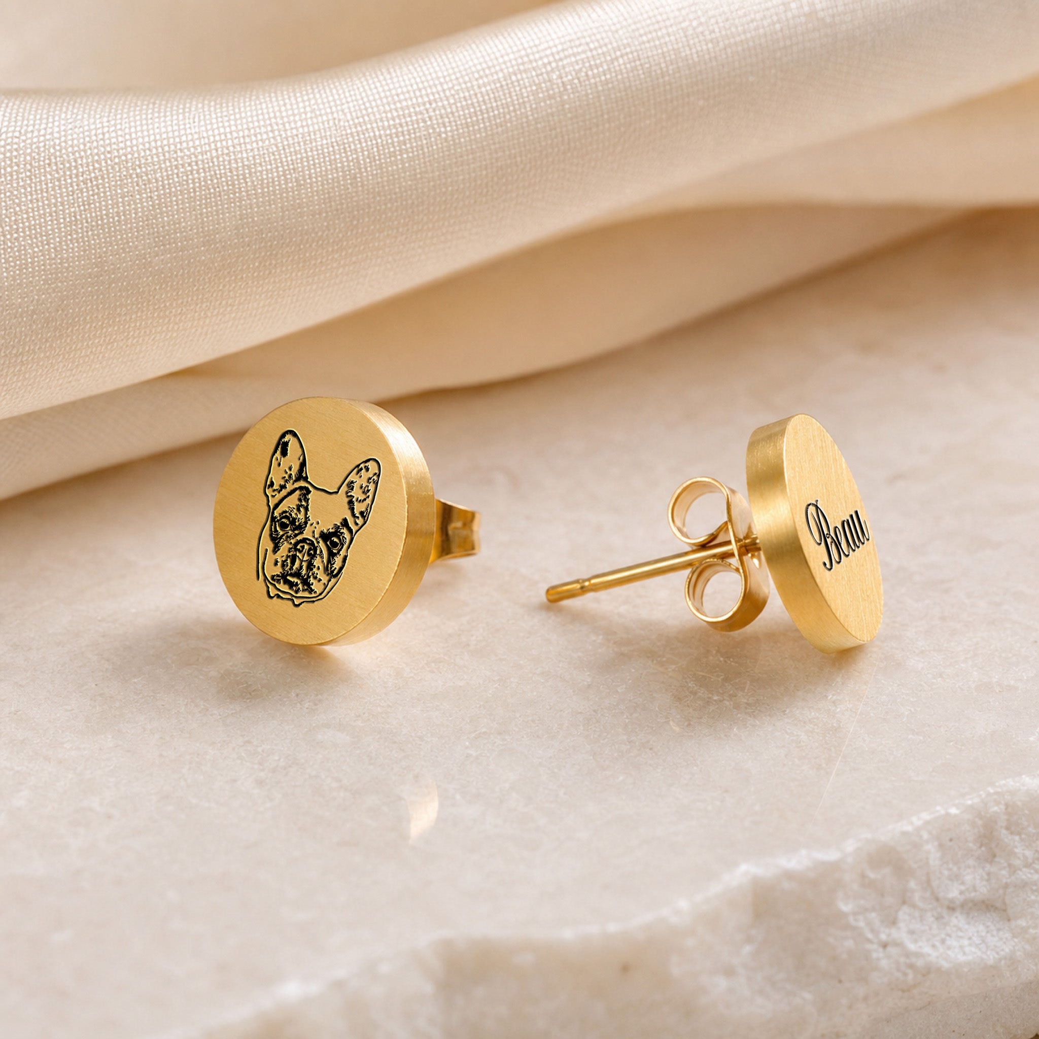 Gold pet portrait stud earrings as a pair, hand-drawn pet portrait on one stud and name in script on the other, on marble