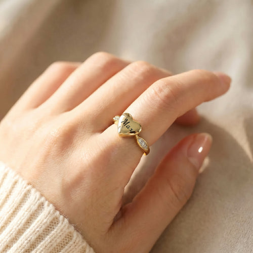 Gold heart urn ring worn on a hand, name engraved on the heart face, CZ stones visible on band shoulders