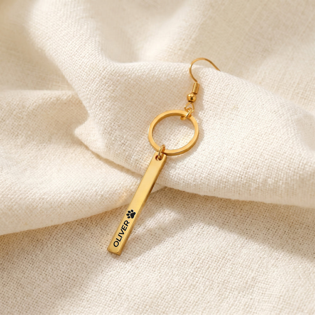 Close-up of a single gold pet name bar drop earring with an engraved name