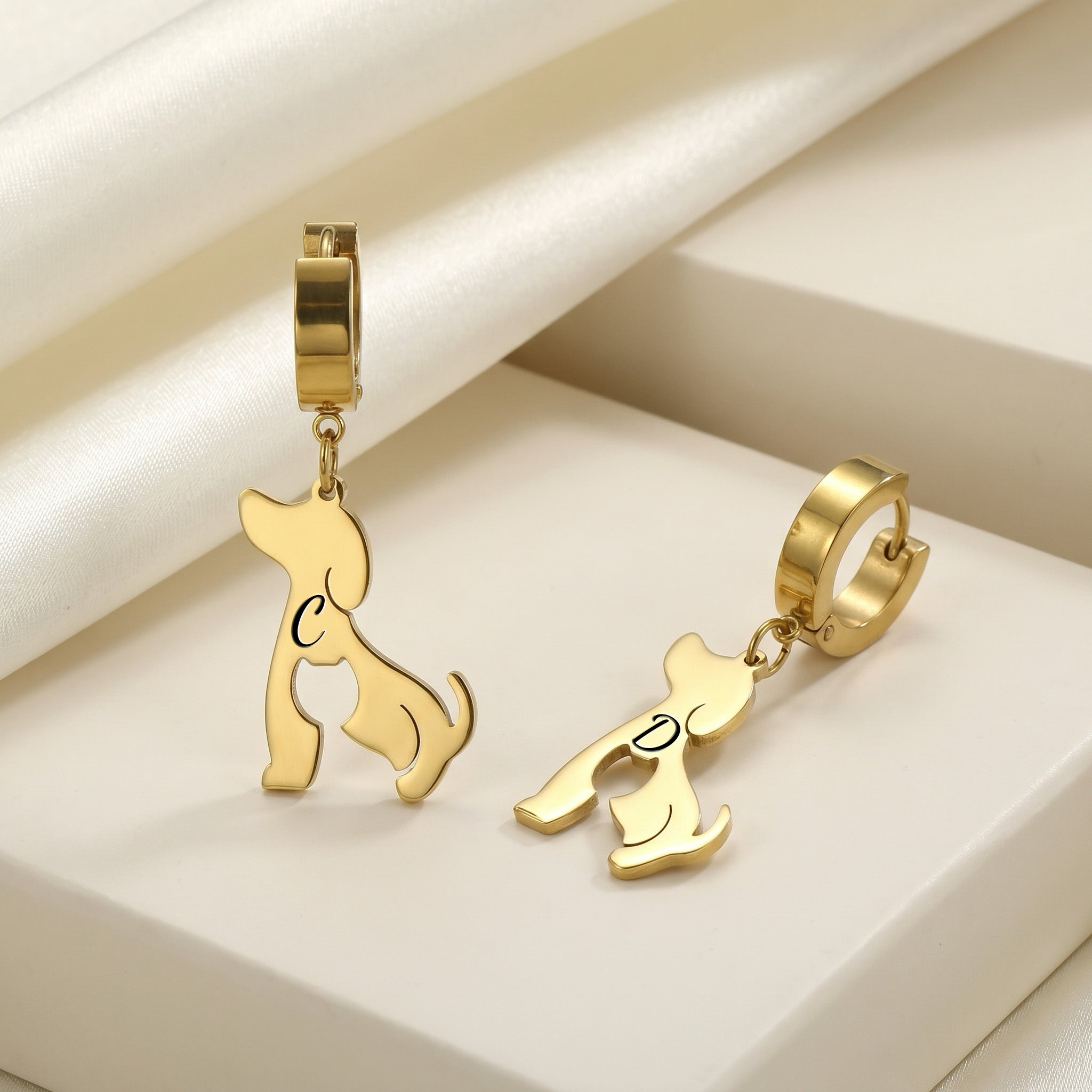 Gold dog-silhouette name earrings displayed on ivory blocks