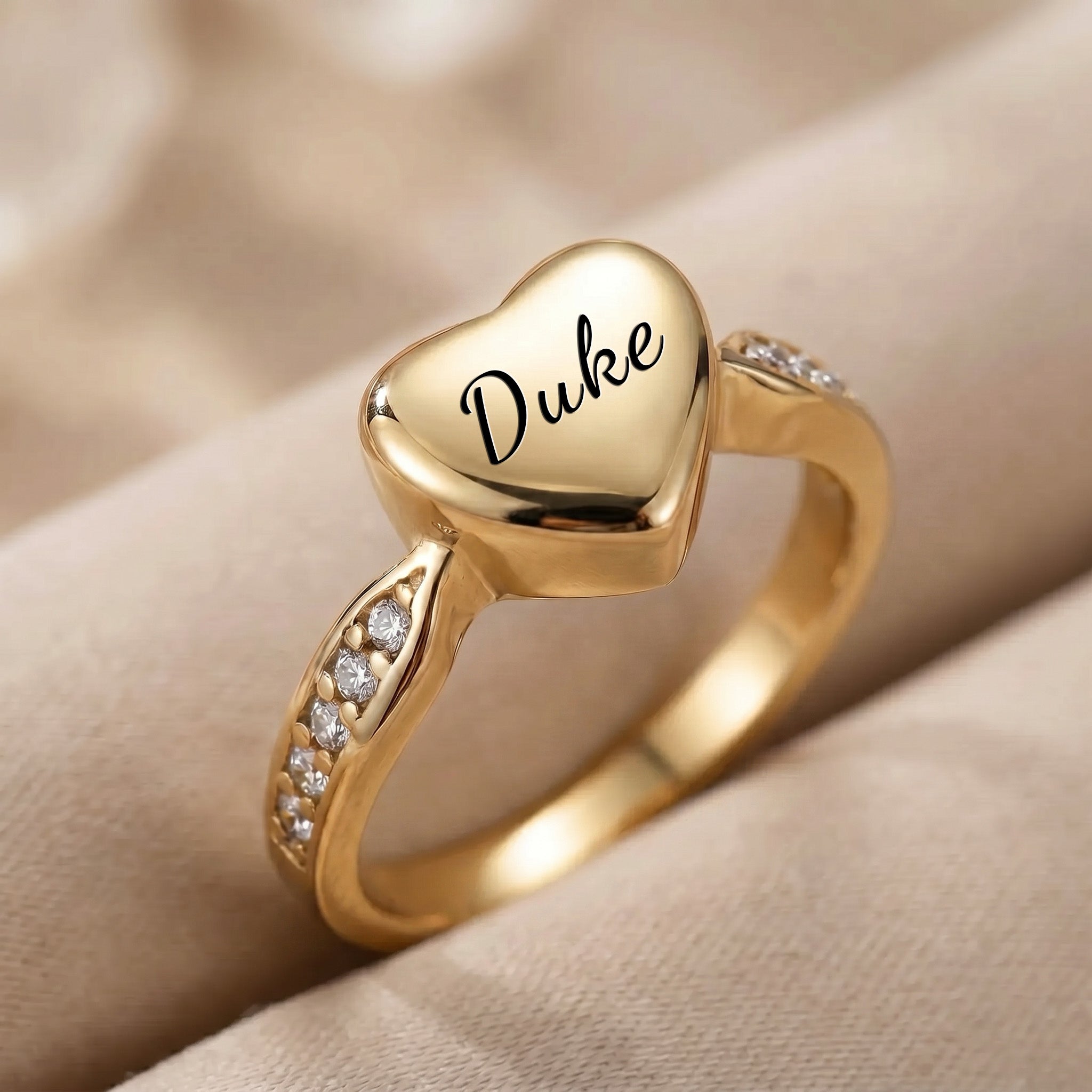 Close-up of gold heart urn ring showing name engraved in script and channel-set CZ stones