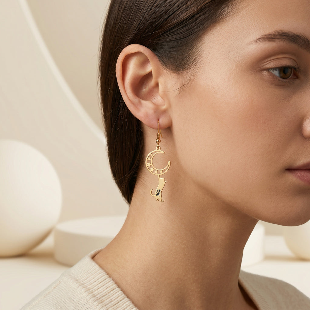 Gold crescent-moon cat drop earring with engraved name worn on the ear, close cropped studio portrait