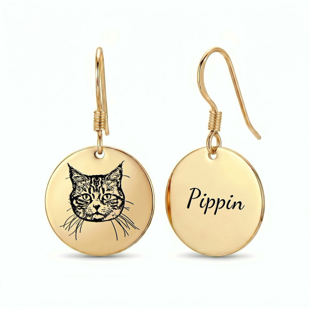 Pair of gold drop earrings with engraved pet portrait and name discs, shown alone on a near-white studio background