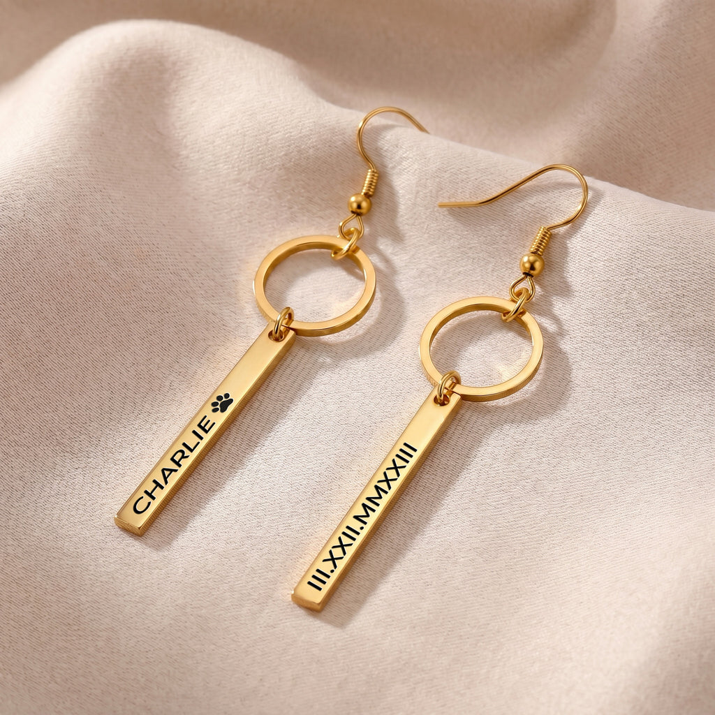 Pair of gold pet name bar drop earrings on softly folded neutral fabric