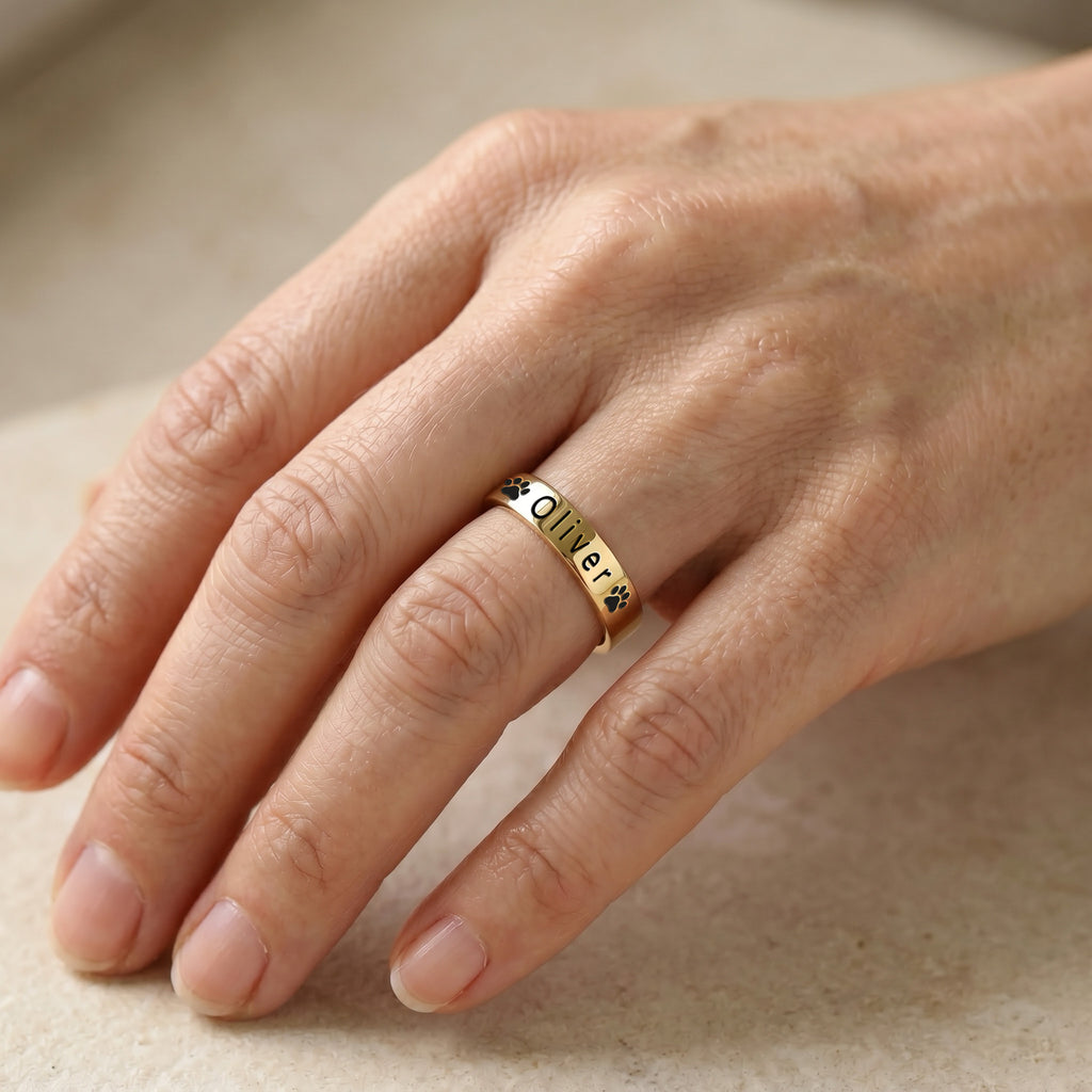 18K gold-plated pet name stacking ring worn on a finger, engraved with a pet's name and paw prints in natural light