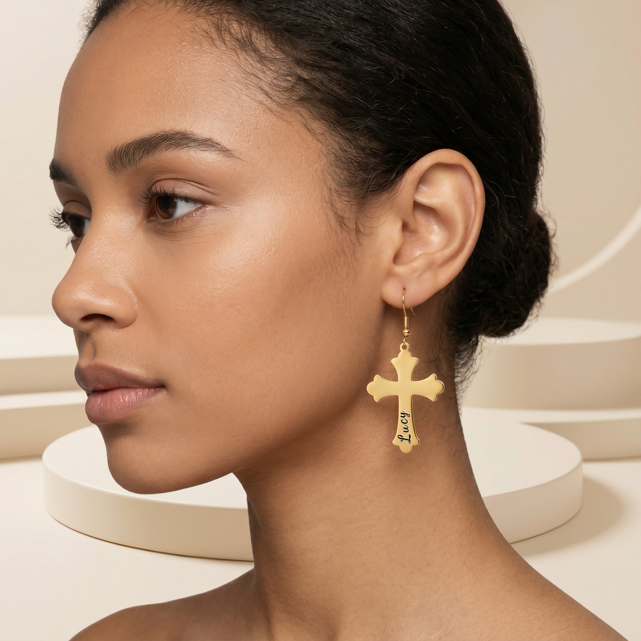 Model wearing a single 18K gold pet cross drop earring engraved with a pet name in script, three-quarter portrait against a soft studio backdrop