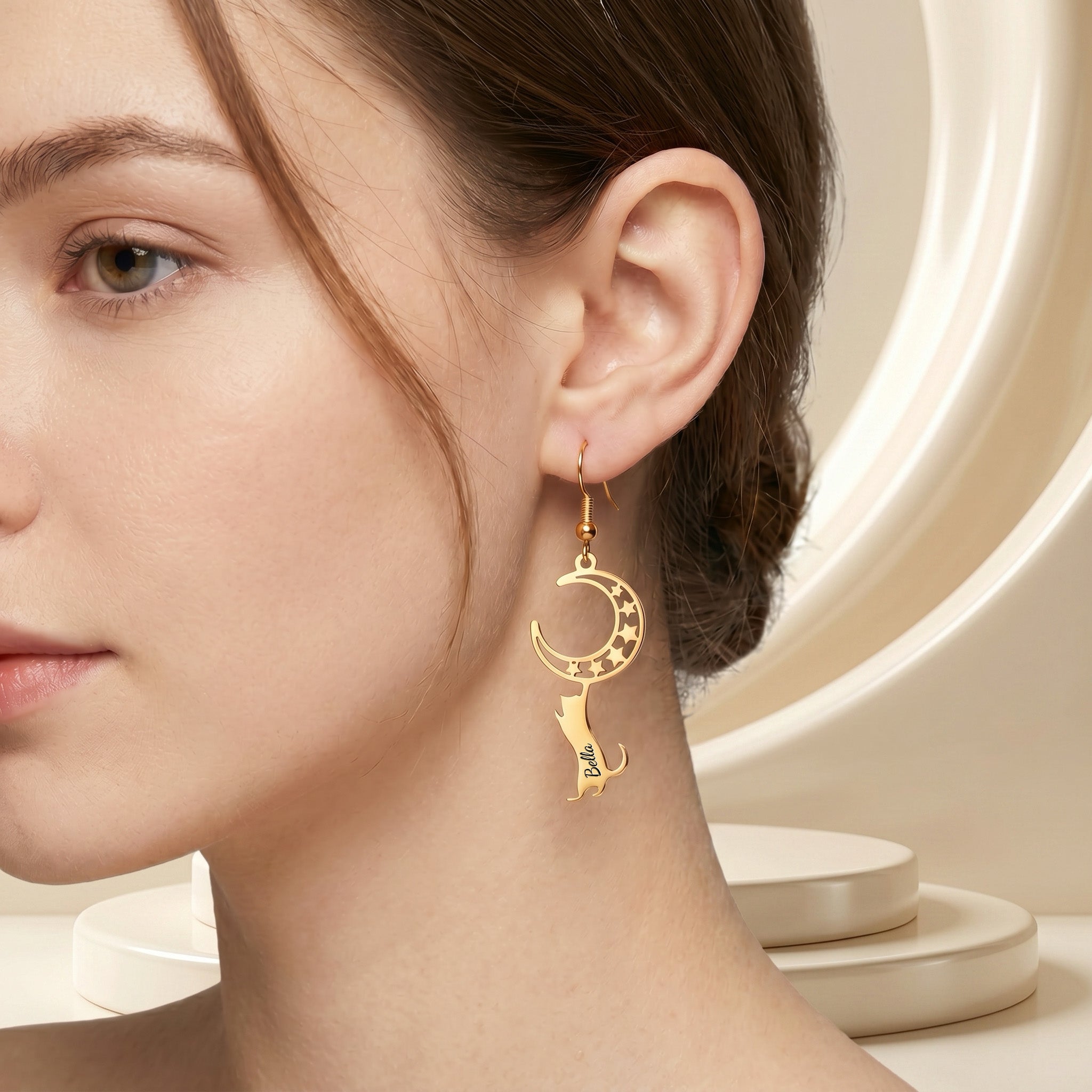 Gold cat-and-moon name drop earring worn in a beauty close-up with hair pinned back