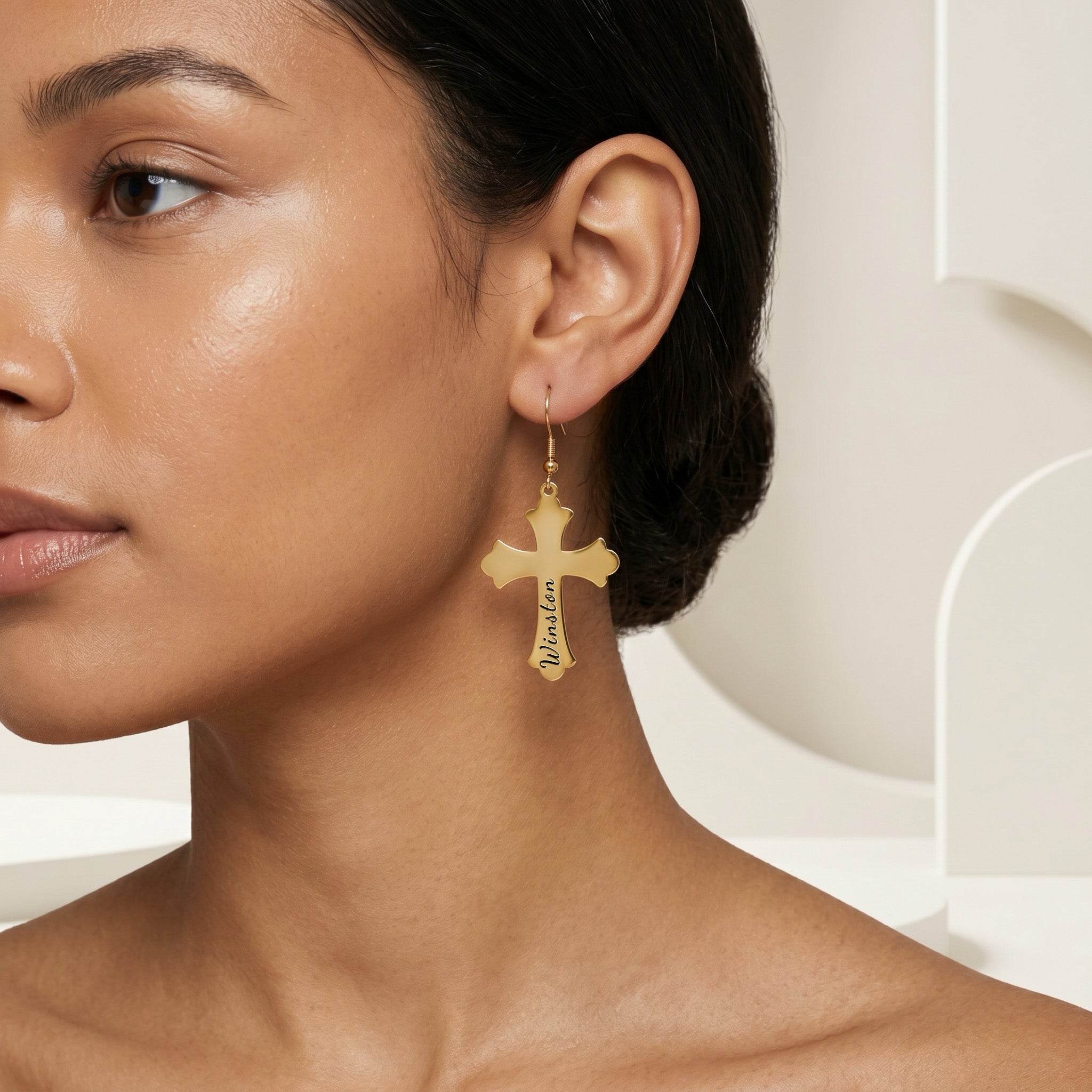 Cropped beauty shot of a model wearing an 18K gold pet cross drop earring in a minimalist set