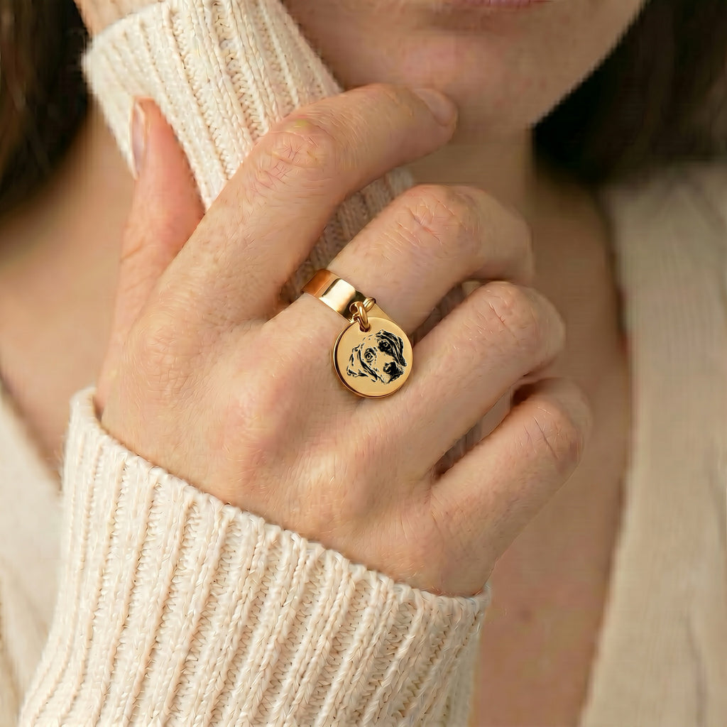 Yellow-gold pet portrait disc ring on a finger, with a cream knit sleeve in a soft indoor crop