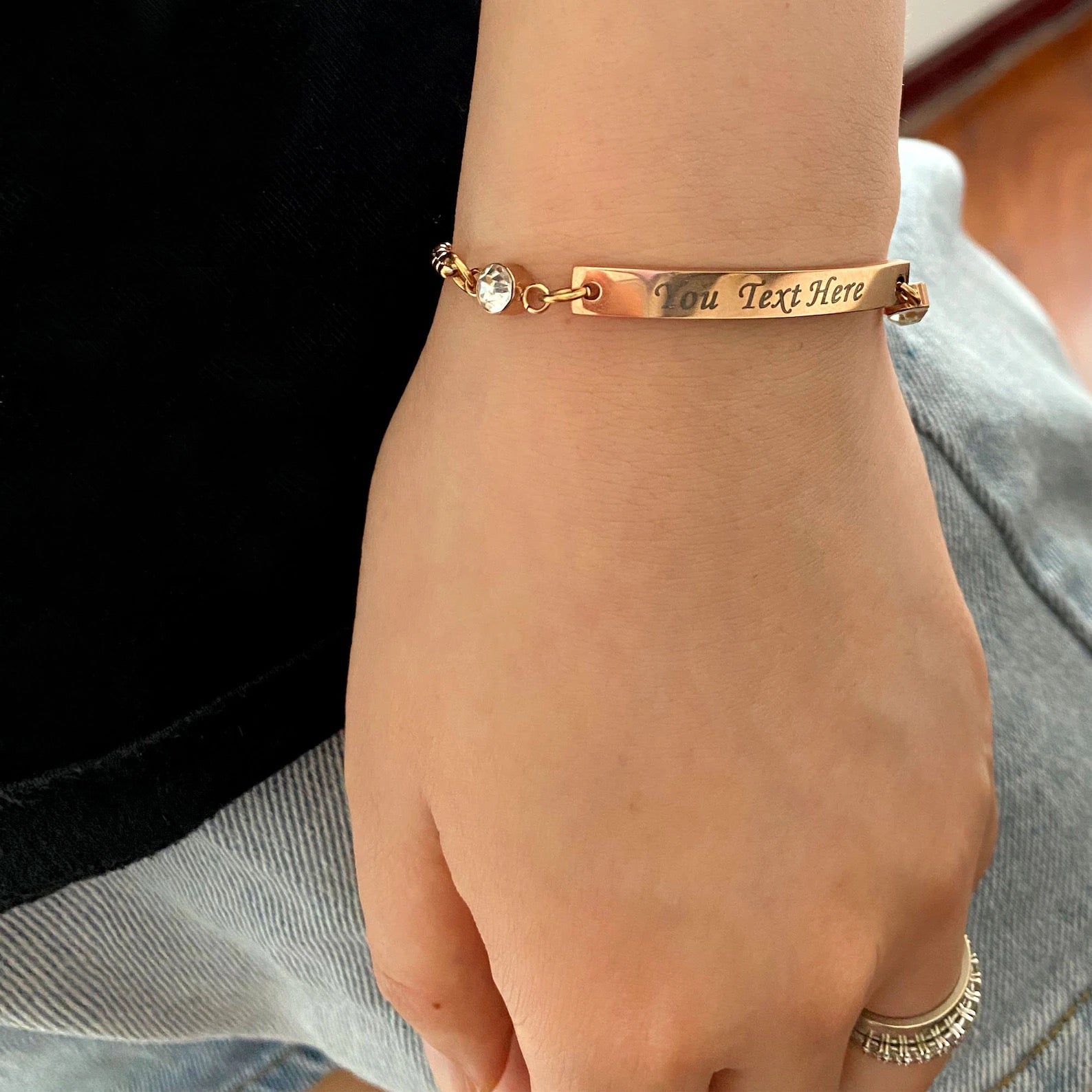 Name bar bracelet on a hand, engraved with custom text and crystal birthstone accents, adjustable chain