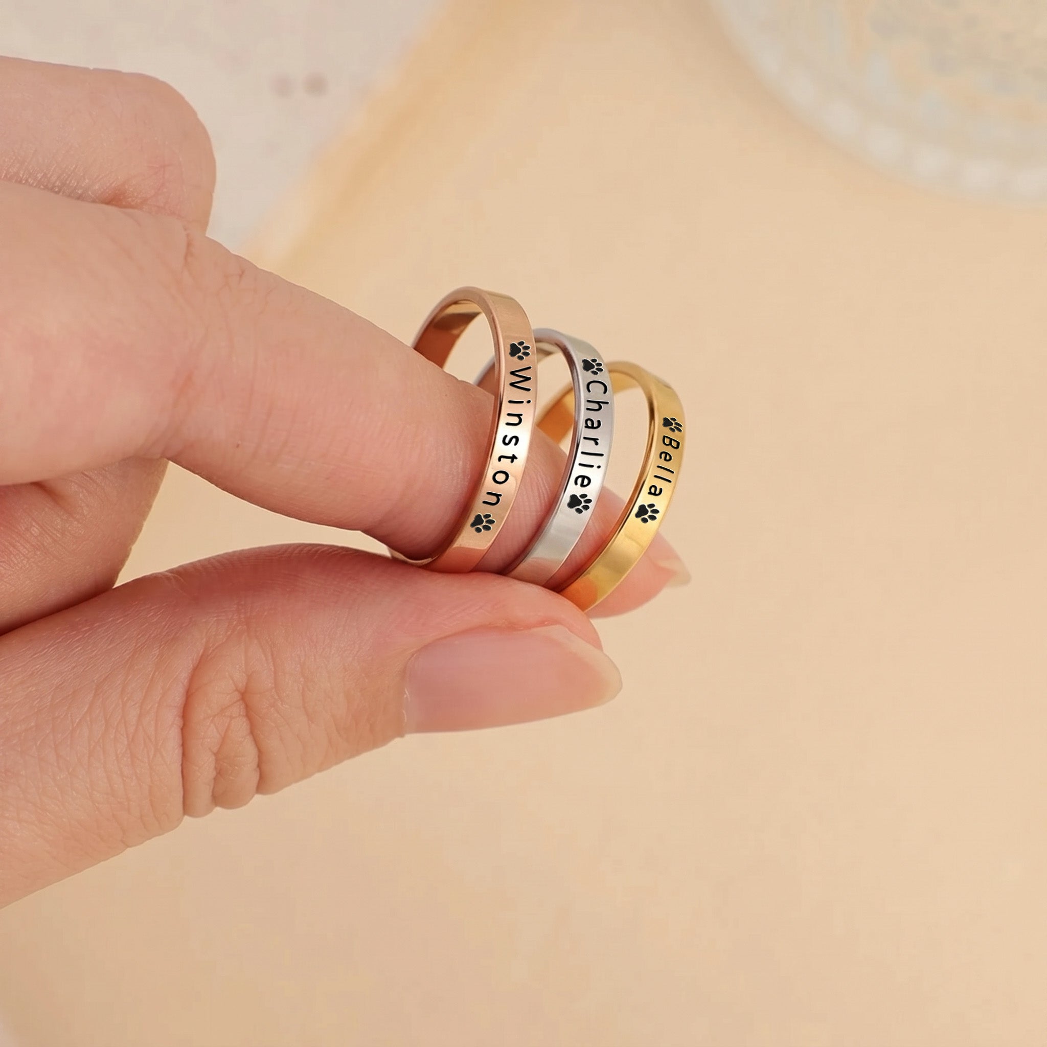 Three pet name band rings in gold, rose gold and silver, engraved with a name and paw, held together to compare finishes