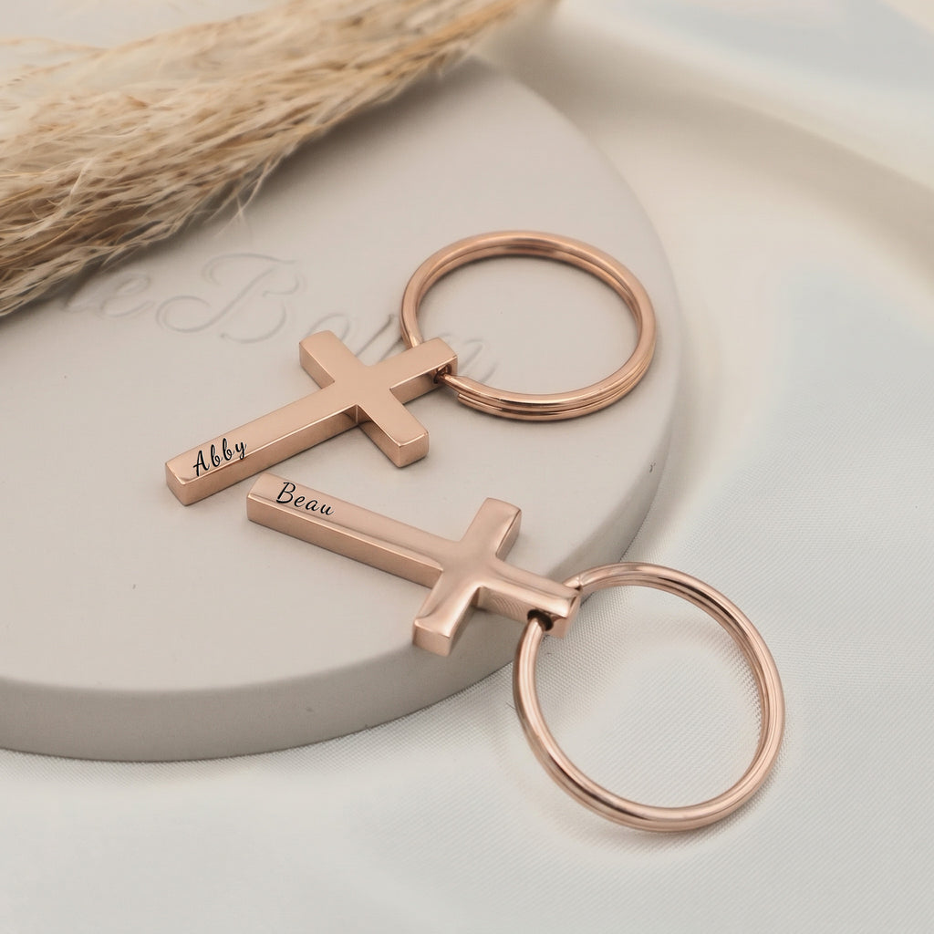18k rose gold pet cross keychain shown as a pair staged on a ceramic tray — hand-drawn portrait + script name engraved on each cross pendant front
