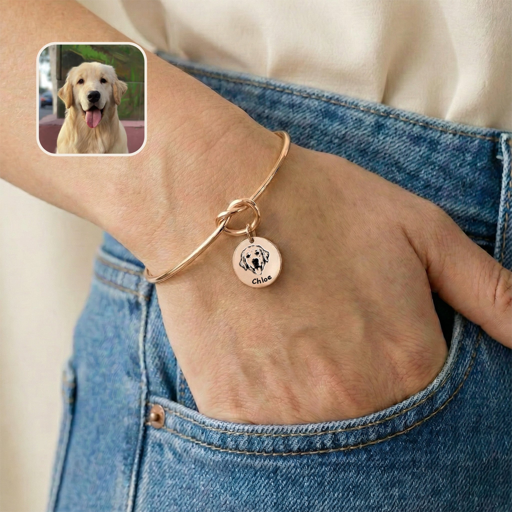 Rose gold knot cuff bracelet with engraved dog portrait charm worn on a wrist, hand resting in a jeans pocket