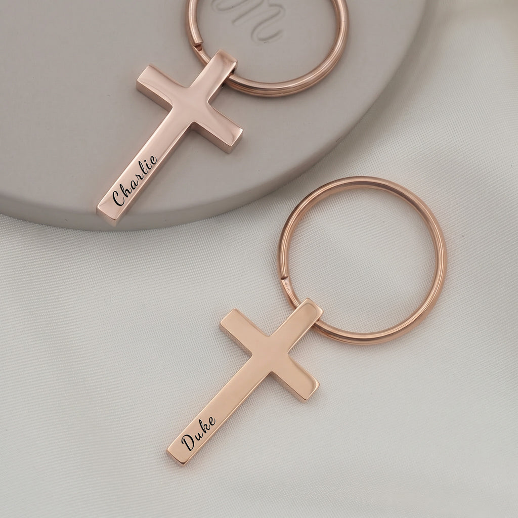 18k rose gold pet cross keychain pair on ceramic tray with soft white fabric — front-face hand-drawn portrait + pet name engraving visible