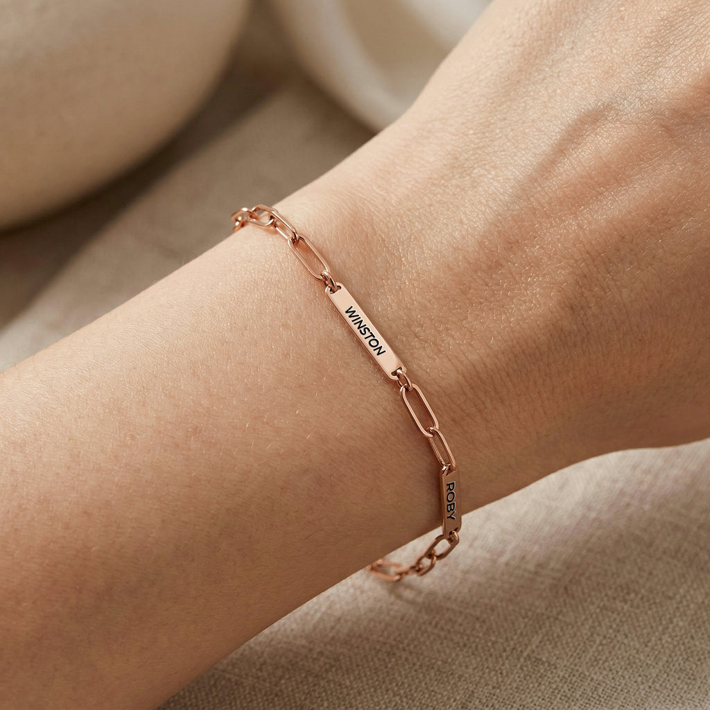 Rose gold paperclip chain pet name bracelet with engraved name bars worn on a wrist in daylight