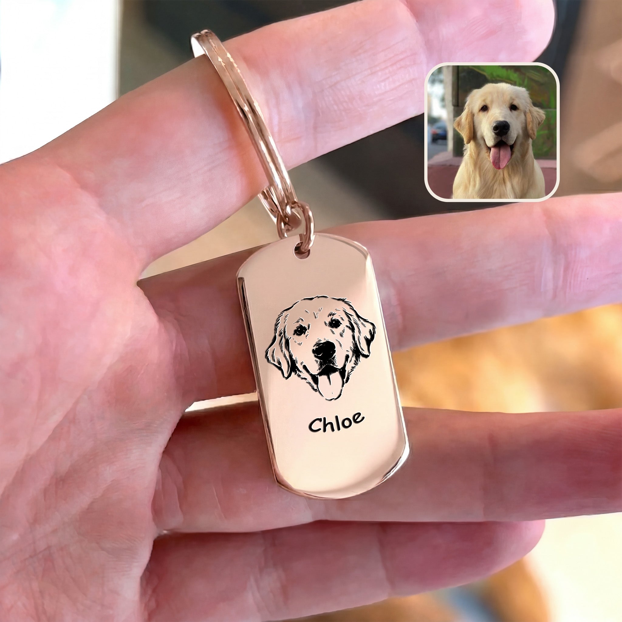 18K rose gold pet portrait dog tag keychain held in hand beside original dog reference photo, warm indoor styled scene