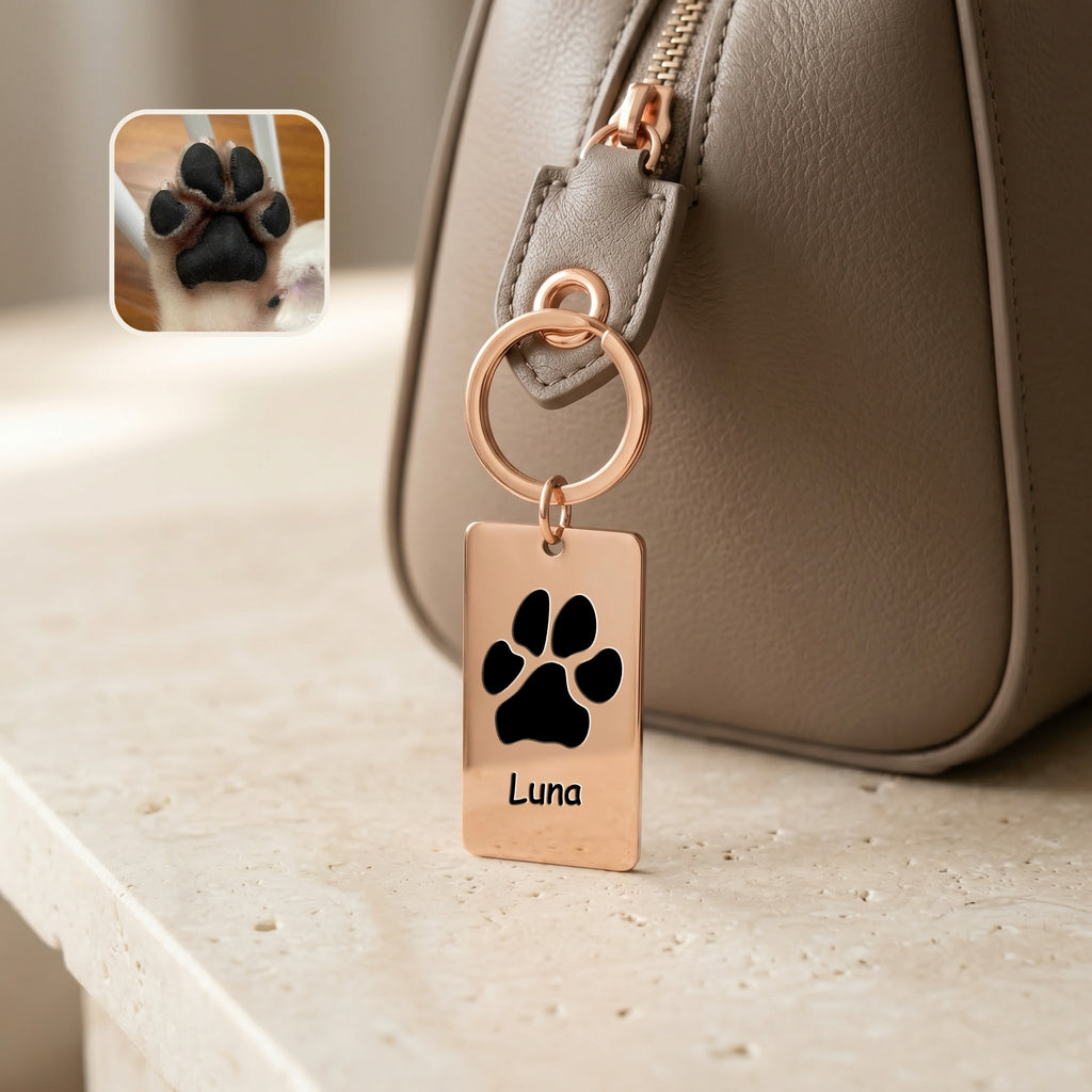18k rose gold plate keychain clipped to a taupe handbag zipper, paw print motif and name 'Luna' engraved on the rectangular plate