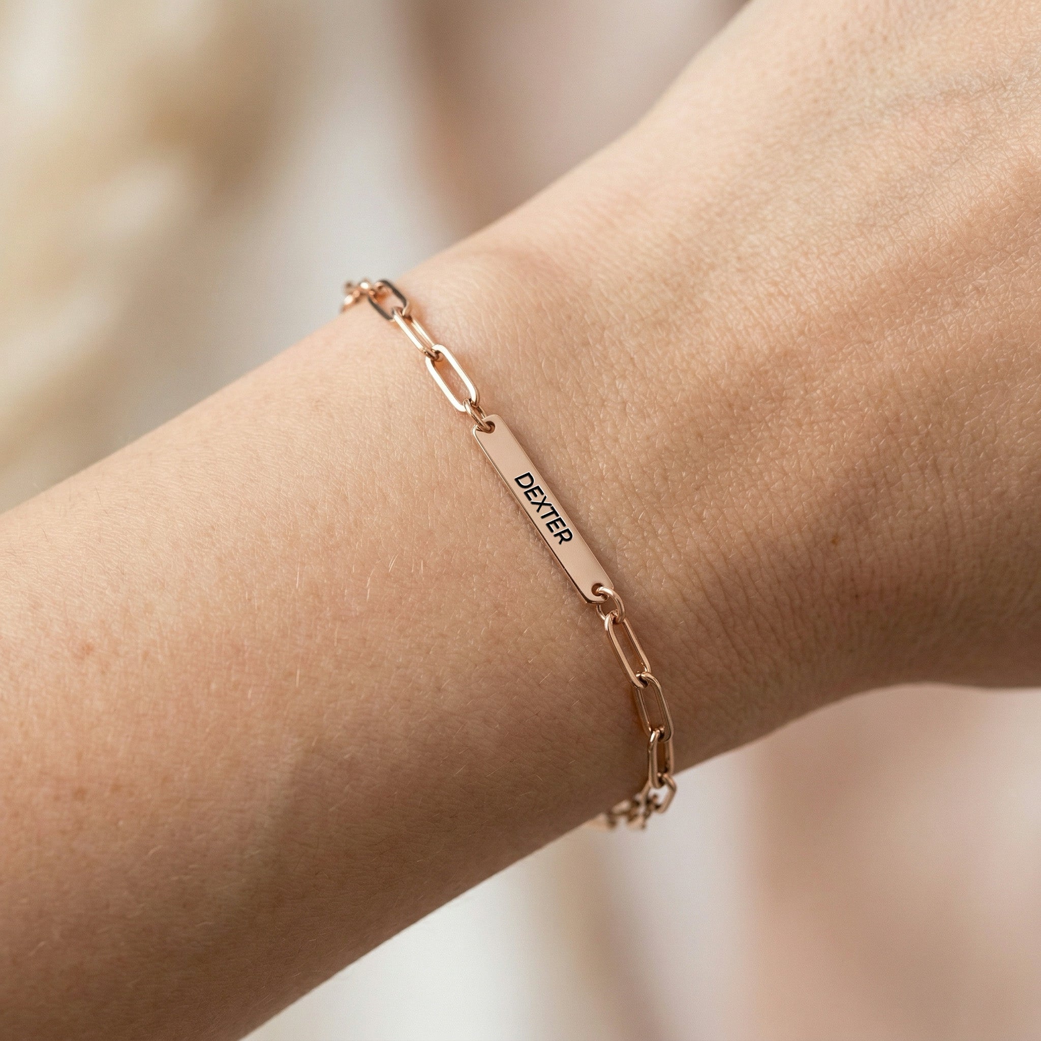 Rose gold paperclip chain pet name bracelet with a single engraved name bar worn on a wrist