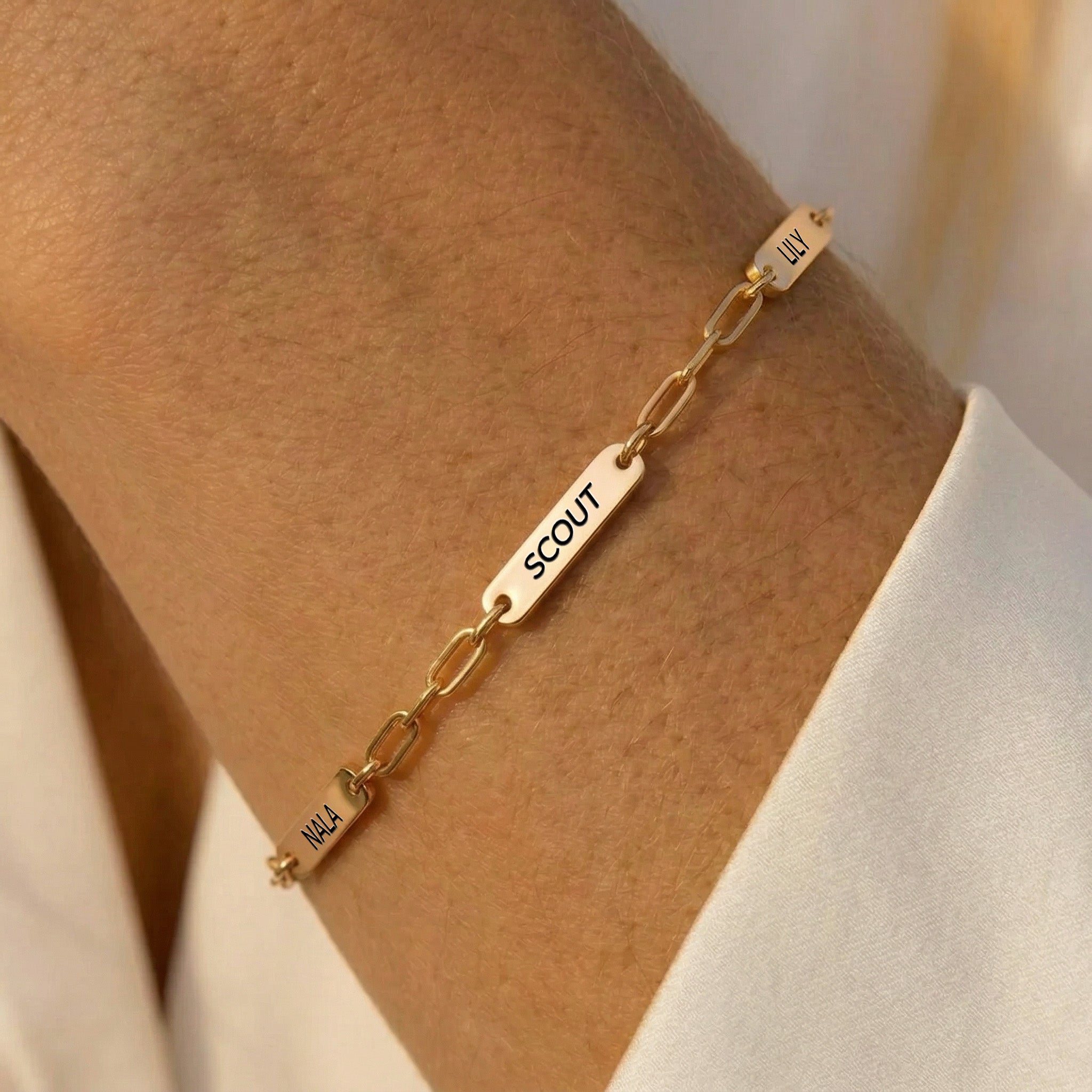 Rose gold paperclip chain pet name bracelet with three engraved name bars worn on a forearm