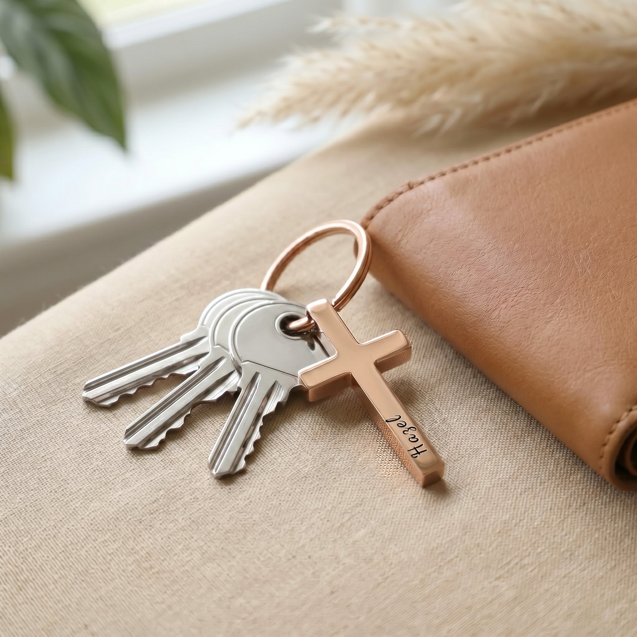 18k rose gold pet cross keychain staged with keys and a brown wallet — everyday-carry pocket scene on neutral surface