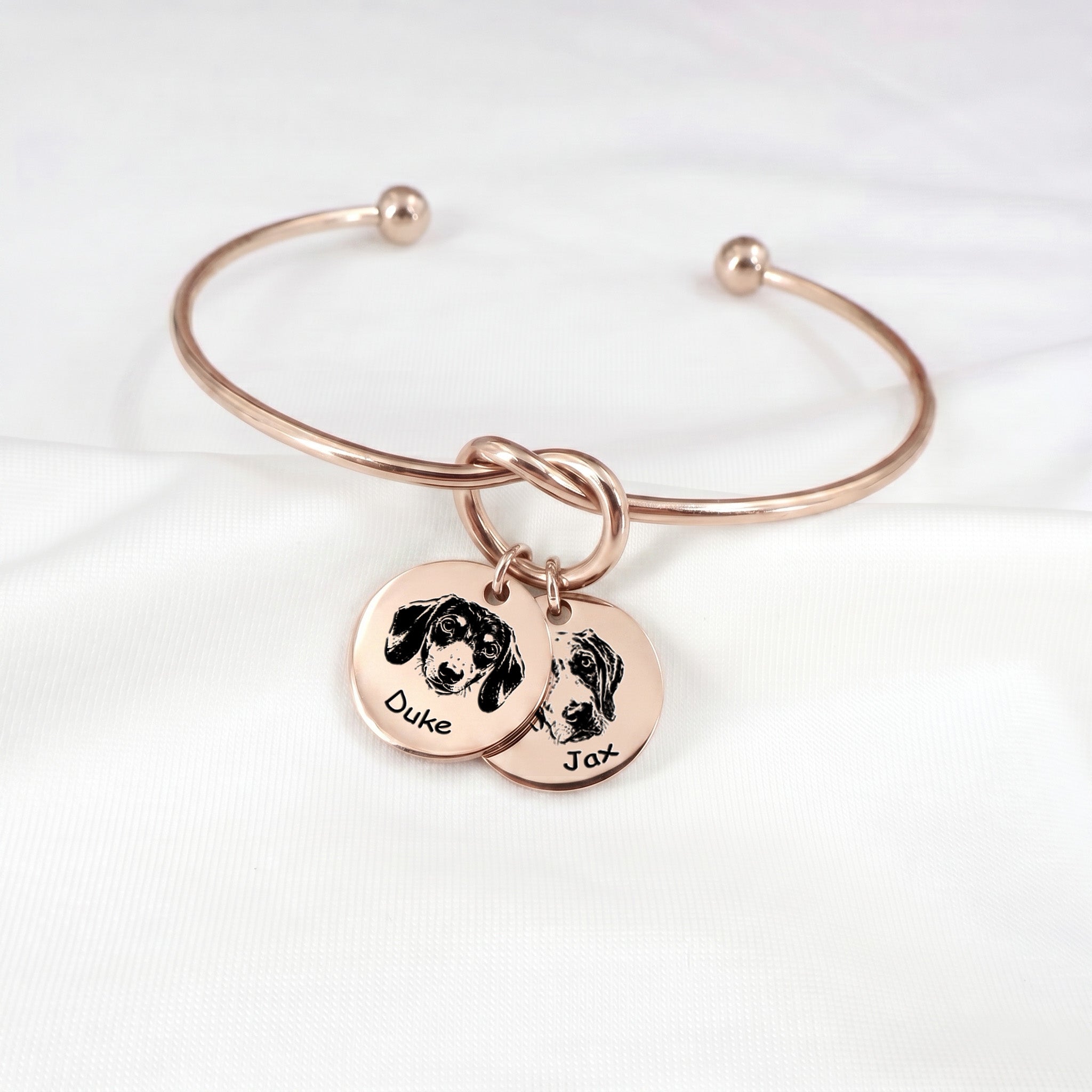 Rose gold knot cuff bracelet with two engraved pet portrait disc charms on a white background