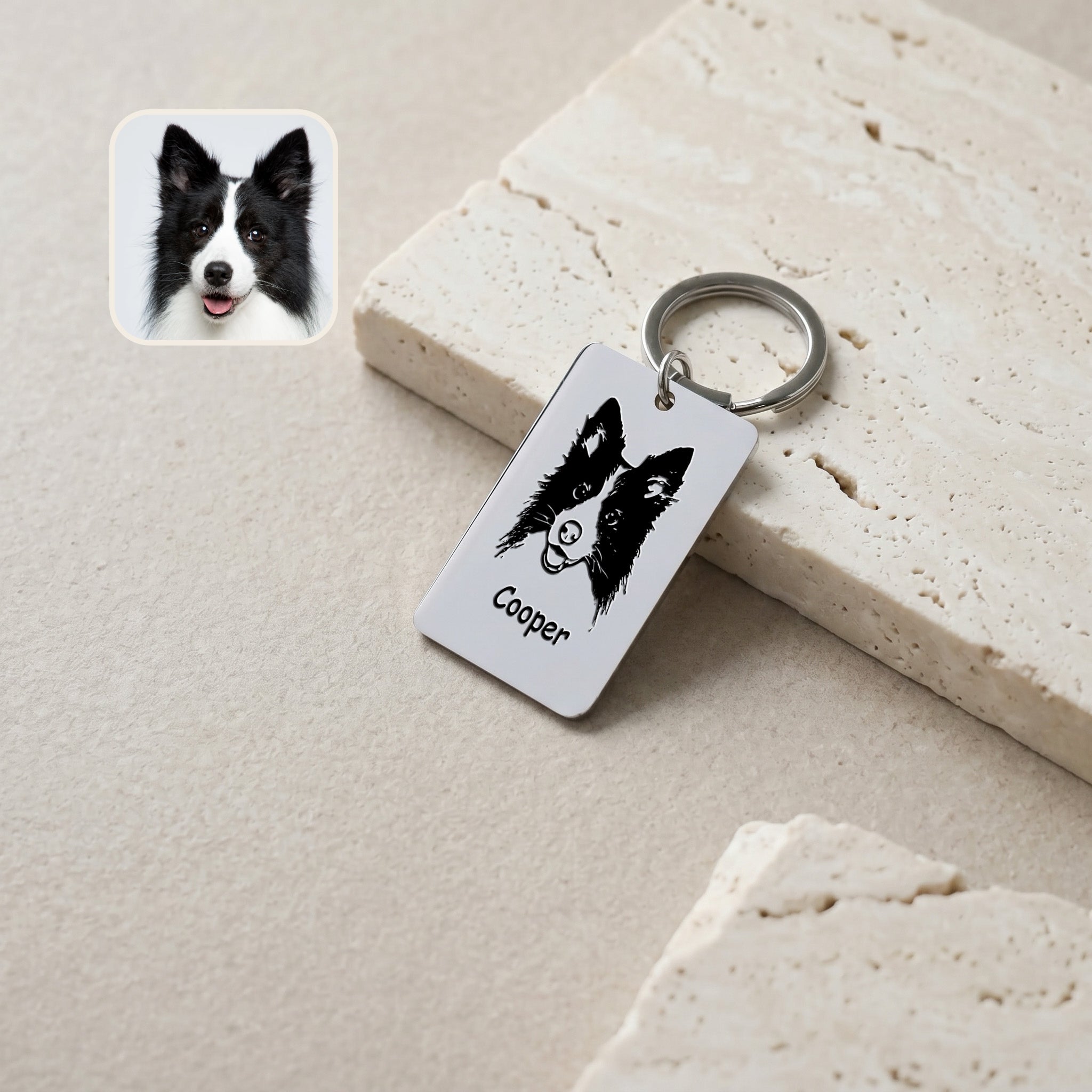 Rhodium pet portrait plate keychain on travertine blocks with a Border Collie reference photo inset, hand-drawn portrait and name 'Cooper' engraved on the rectangular plate