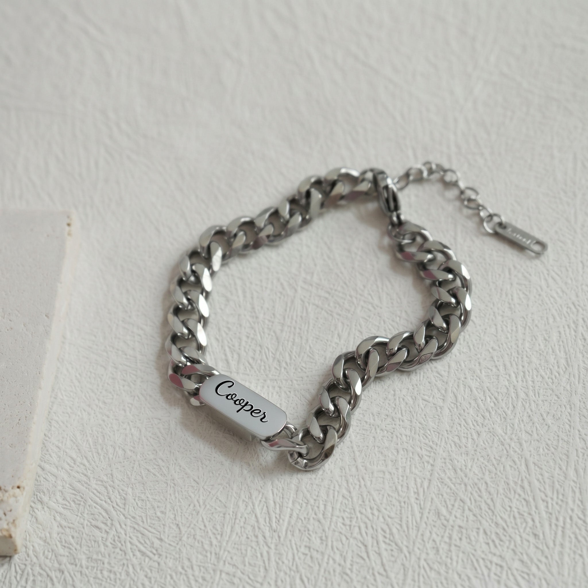 Rhodium silver curb-chain pet name bracelet with an engraved oval nameplate on a neutral surface
