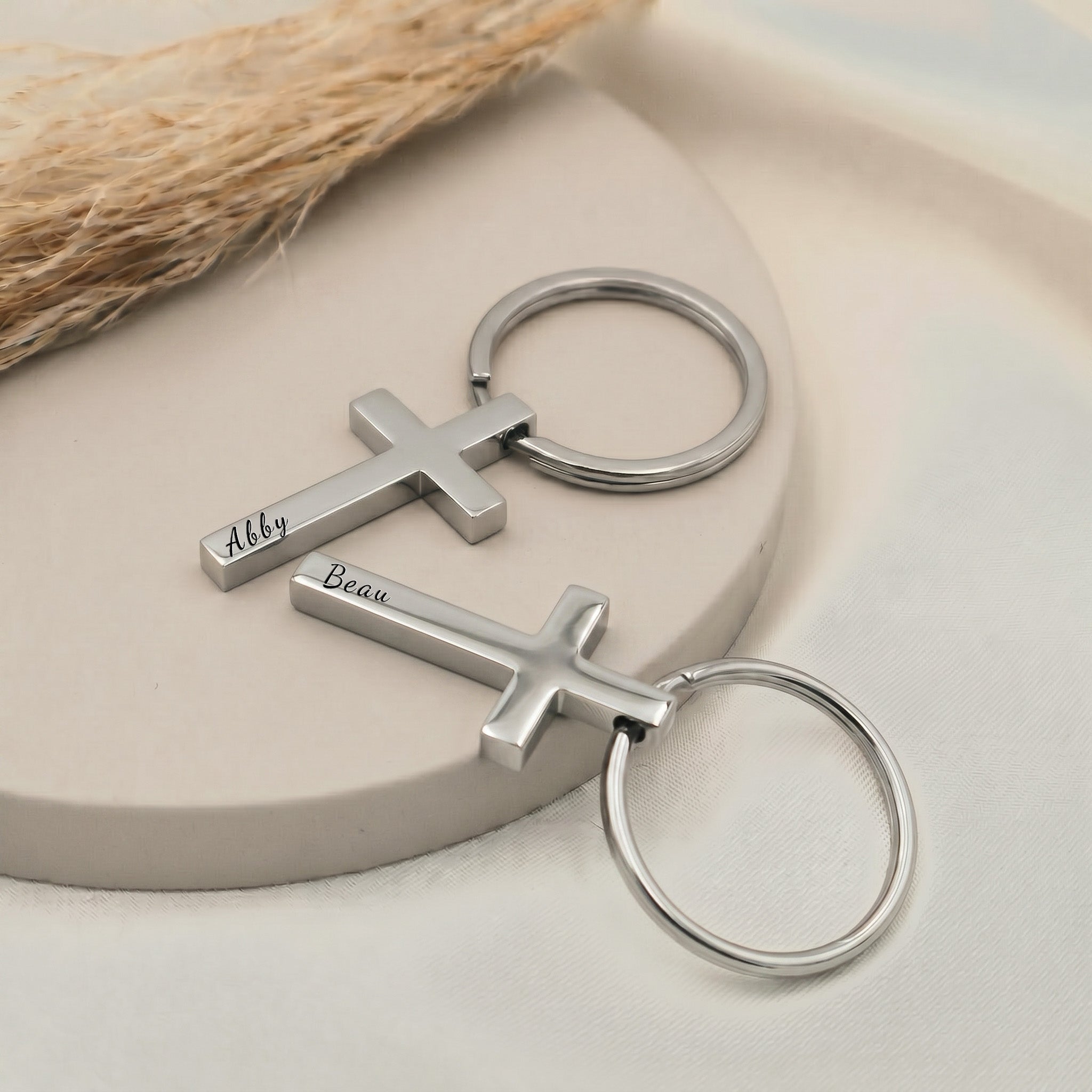 Rhodium pet cross keychain shown as a pair staged on a ceramic tray — hand-drawn portrait + script name engraved on each cross pendant front