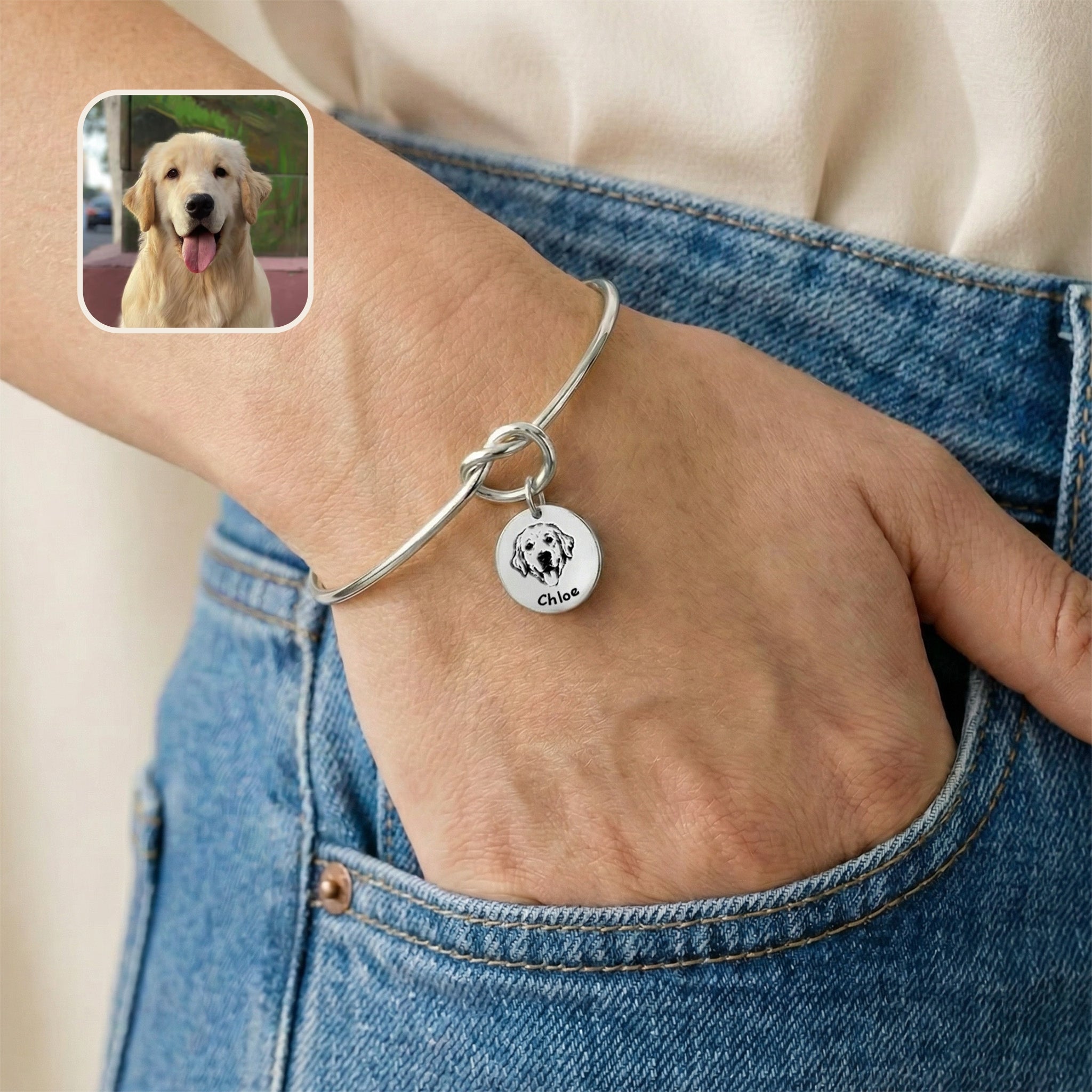 Silver rhodium knot cuff bracelet with engraved dog portrait charm worn on a wrist, hand in a jeans pocket