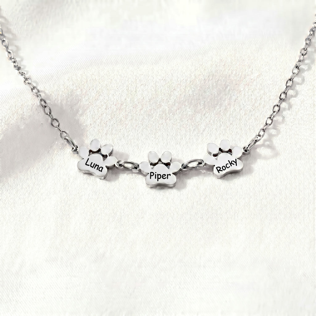 Three silver paw name charms linked along a bracelet chain in a flat lay