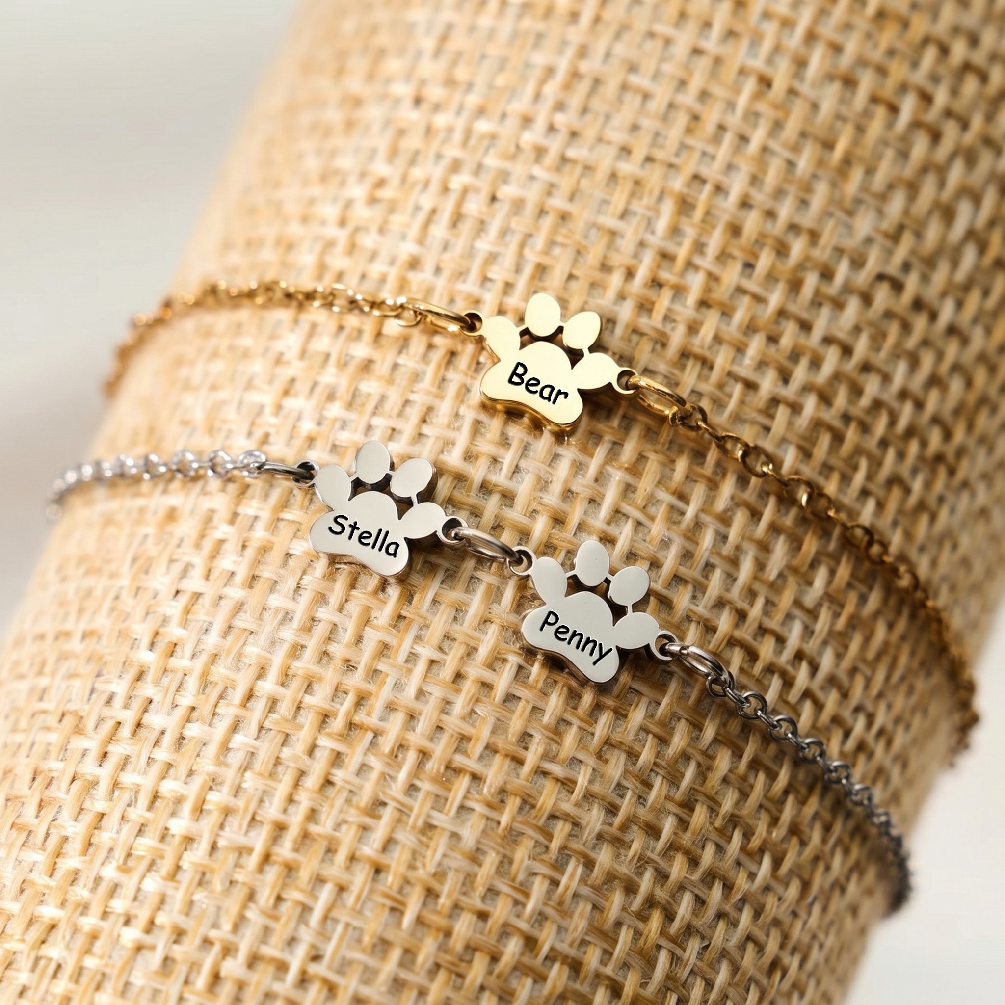 Gold and silver paw name bracelets displayed together on a woven prop