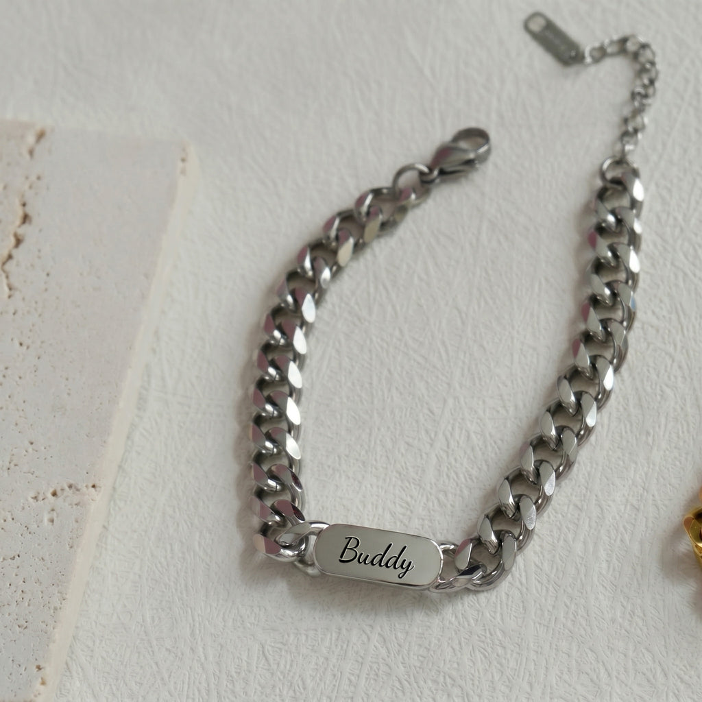 Rhodium silver pet name bracelet laid flat, a name engraved in script on the oval plate